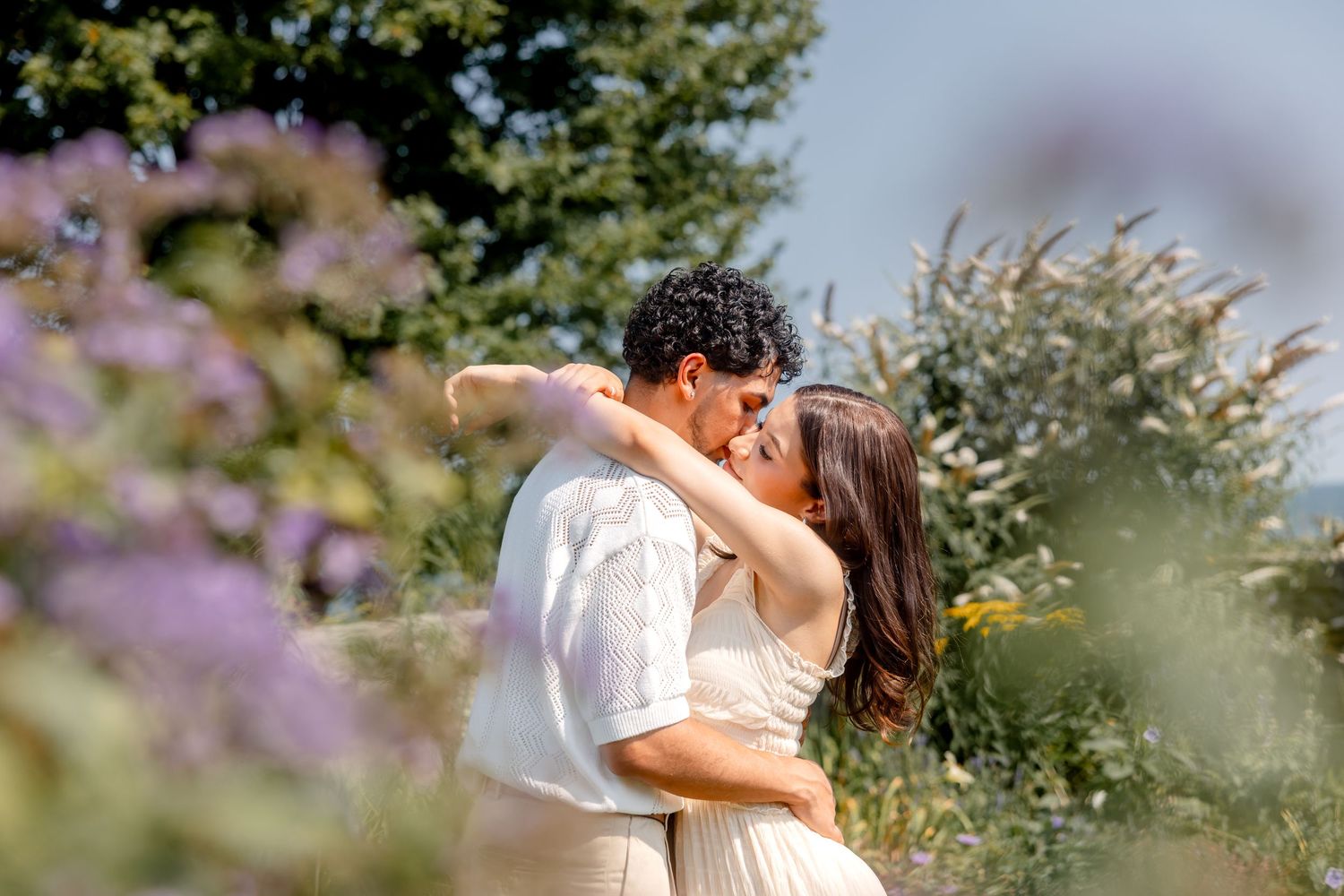 Romantic couple embraces in a blooming garden with soft purple flowers in the background.