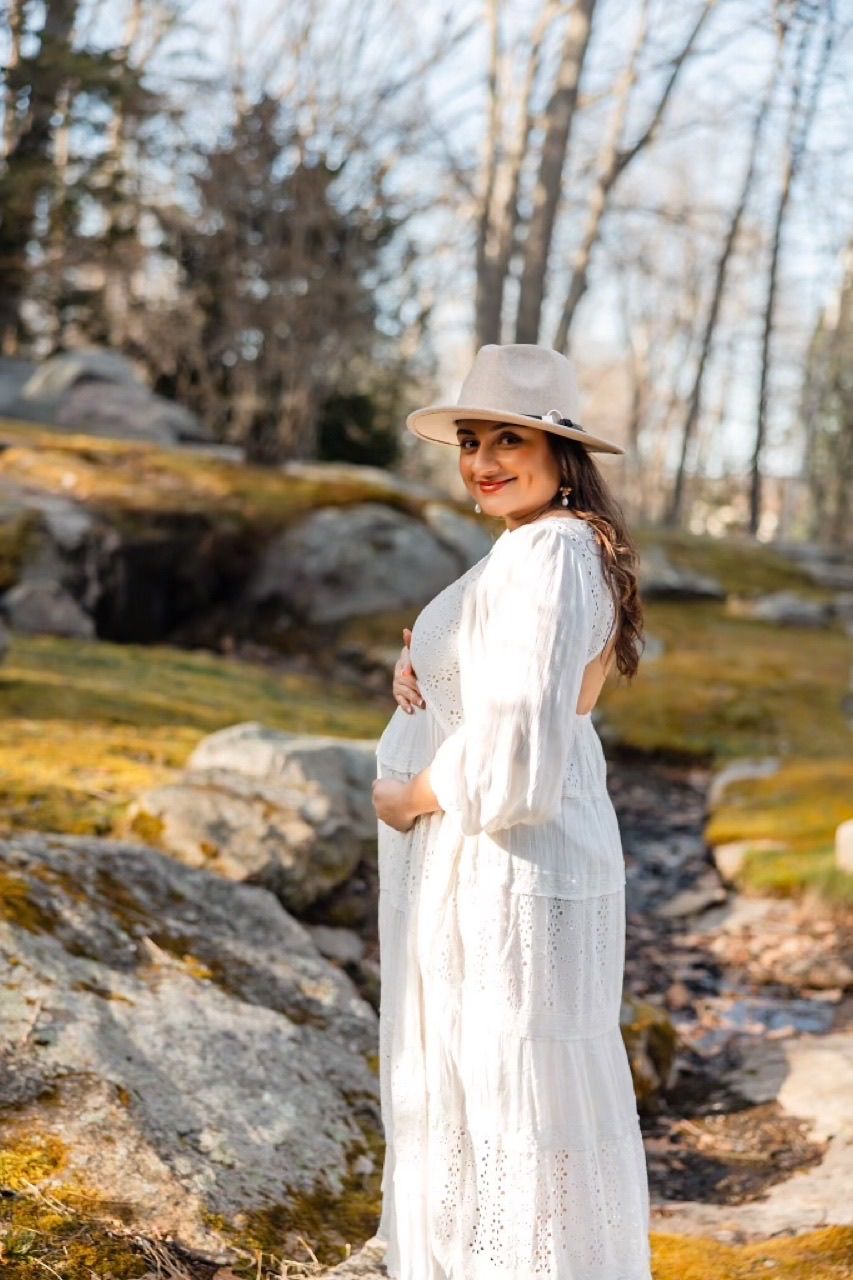 Figure in flowing white dress poses among rocky terrain and moss-covered stones.