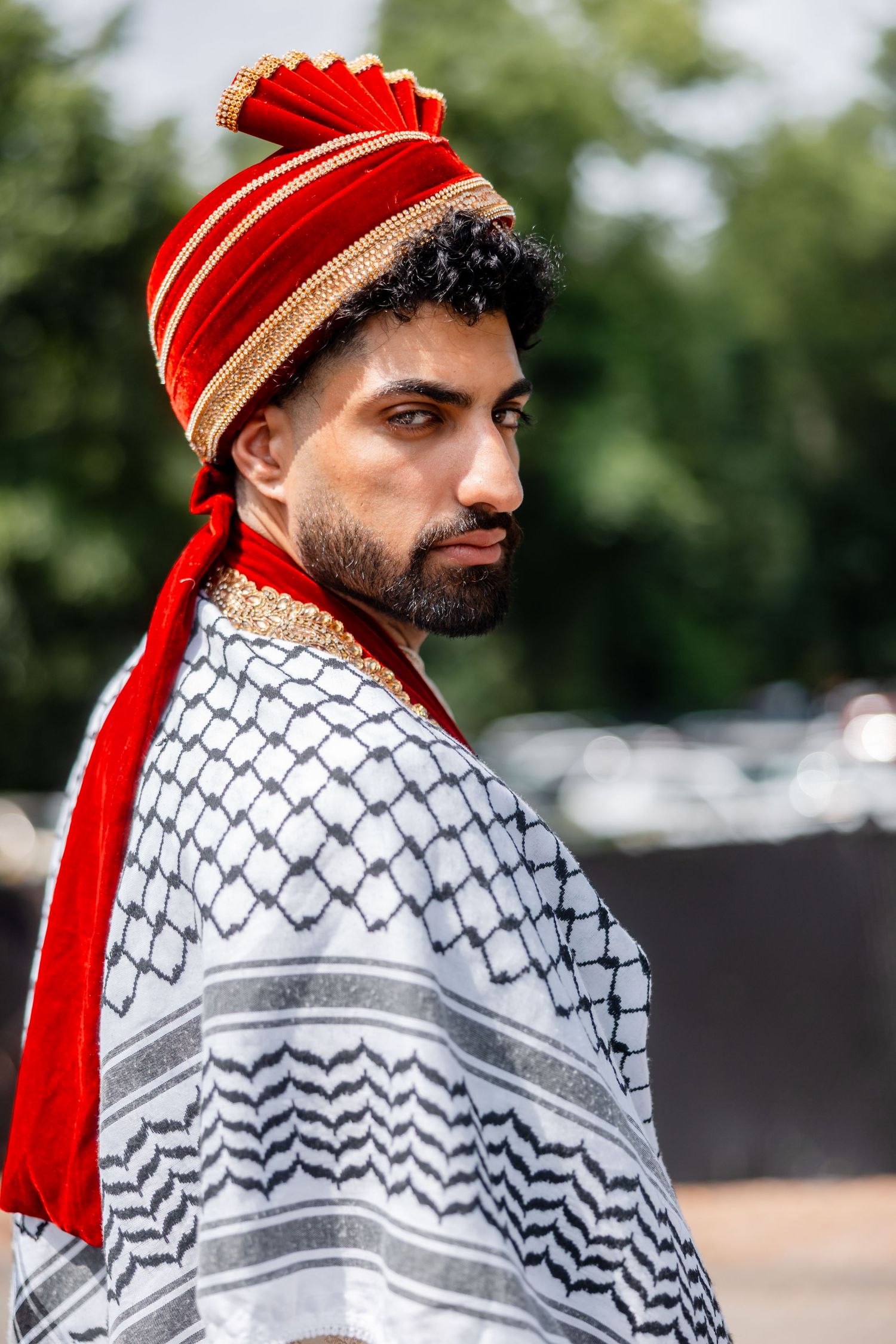 Groom wearing traditional red turban and patterned shawl in cultural wedding attire.