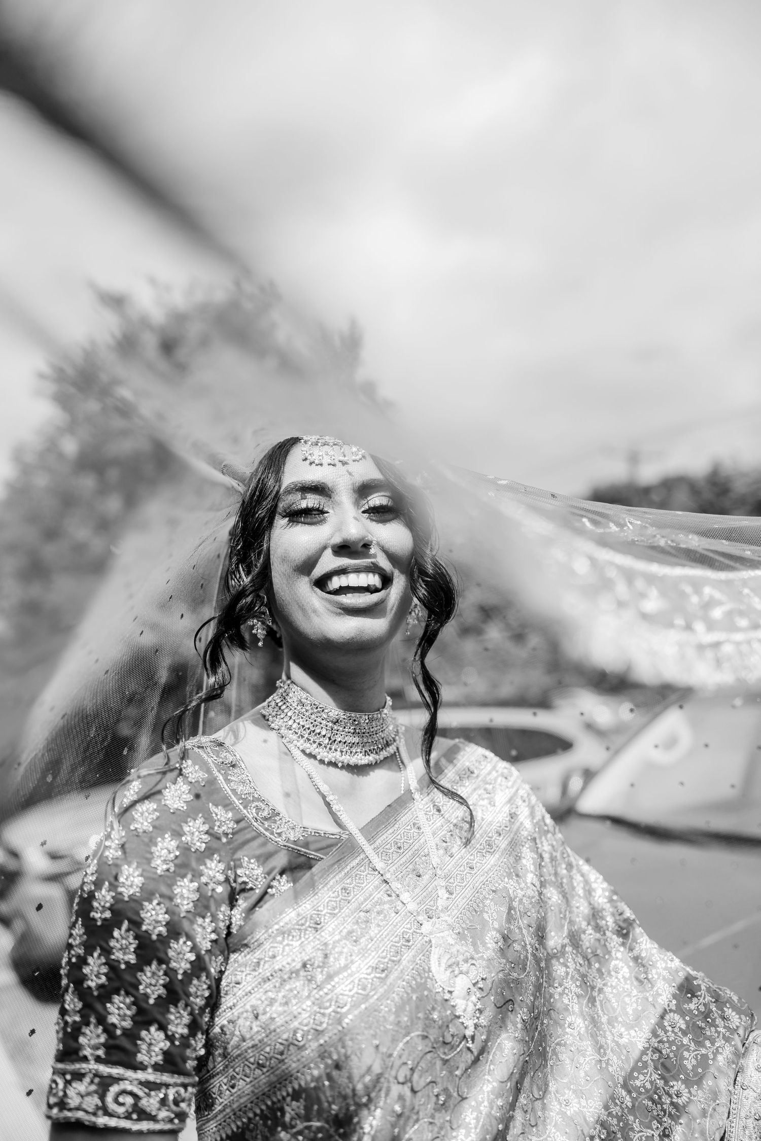 Black and white portrait of bride in traditional South Asian attire with ornate jewelry and headpiece.