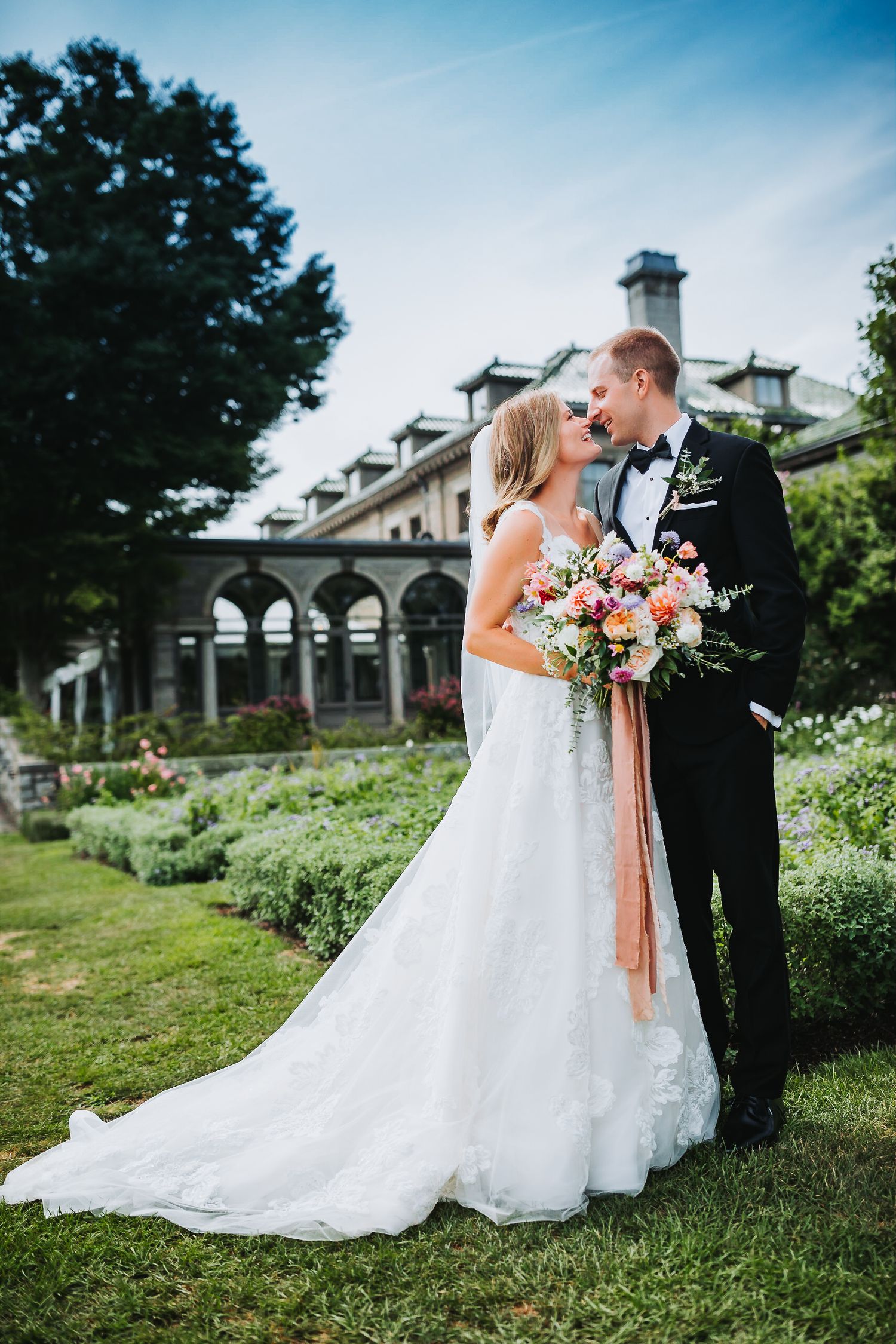 Bride and groom kissing in garden setting, bride holding floral bouquet in white lace wedding dress