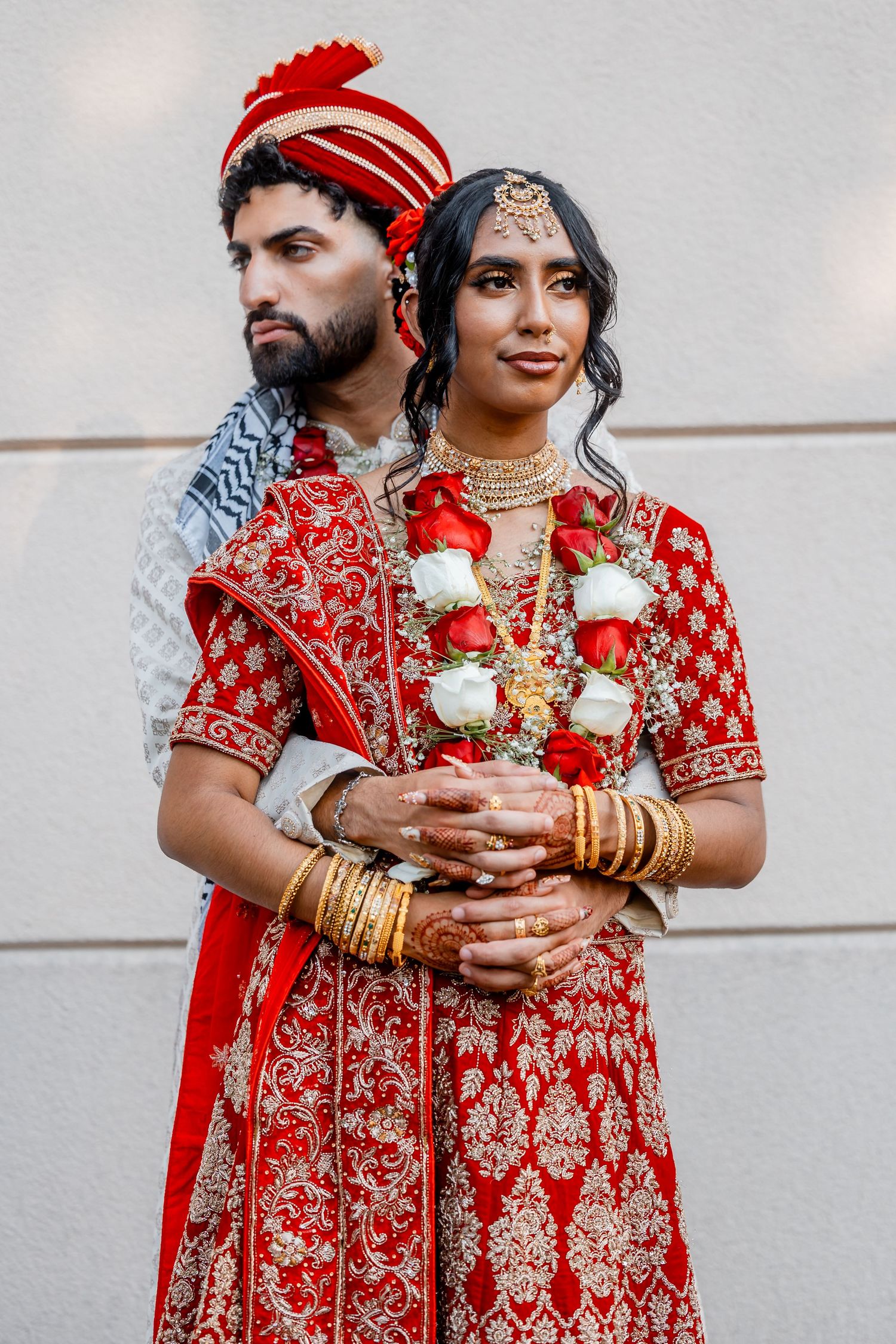 A couple in traditional Indian wedding attire pose together, with the bride in a detailed red lehenga.