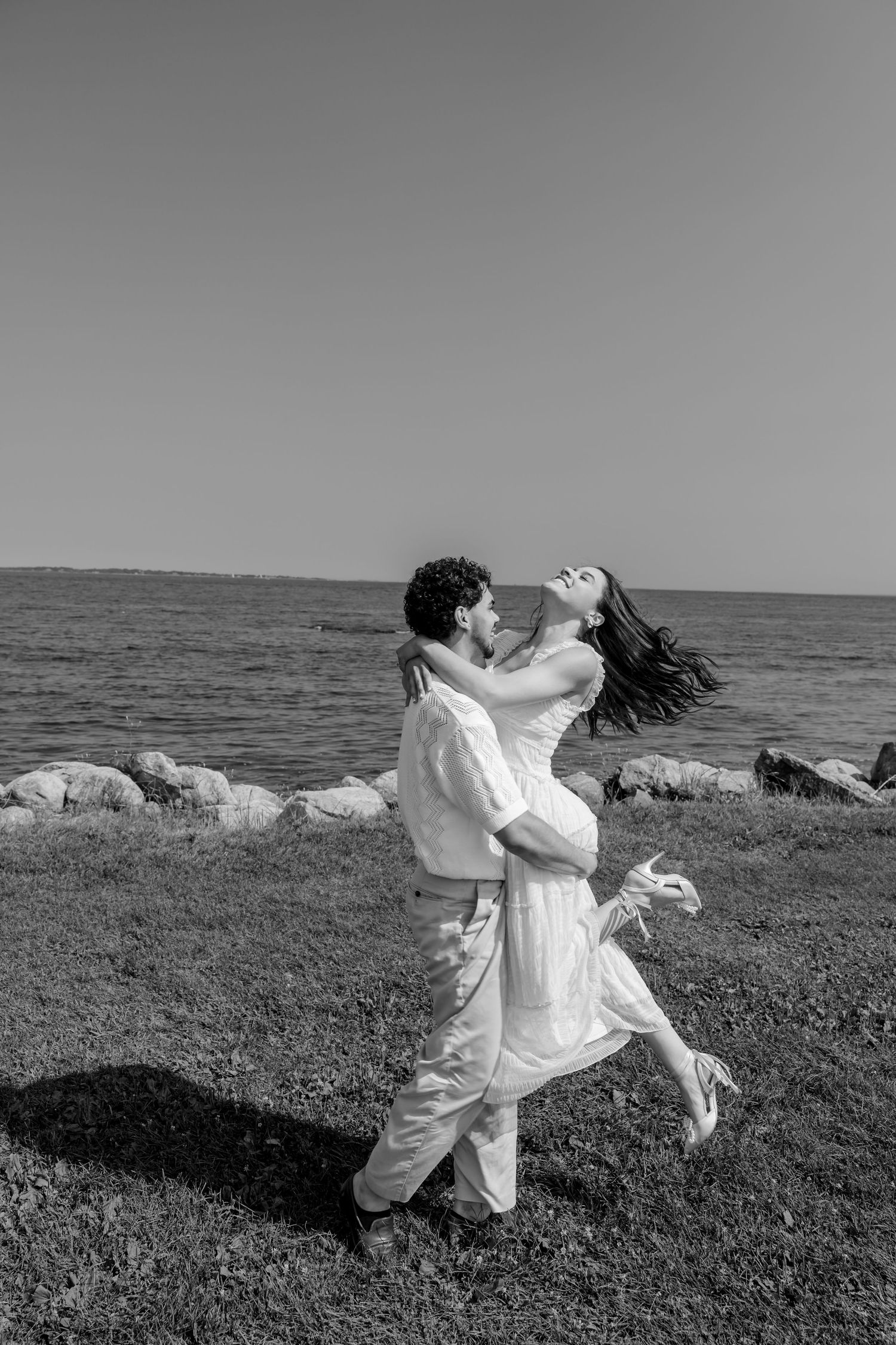 Couple in white clothing dancing and spinning together on a grassy cliff by the ocean.