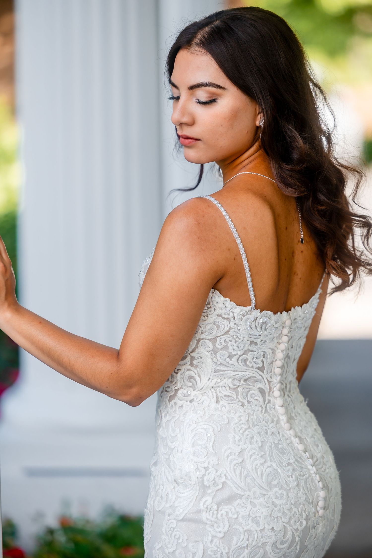 Back view of a fitted lace wedding gown with thin straps against an outdoor backdrop.