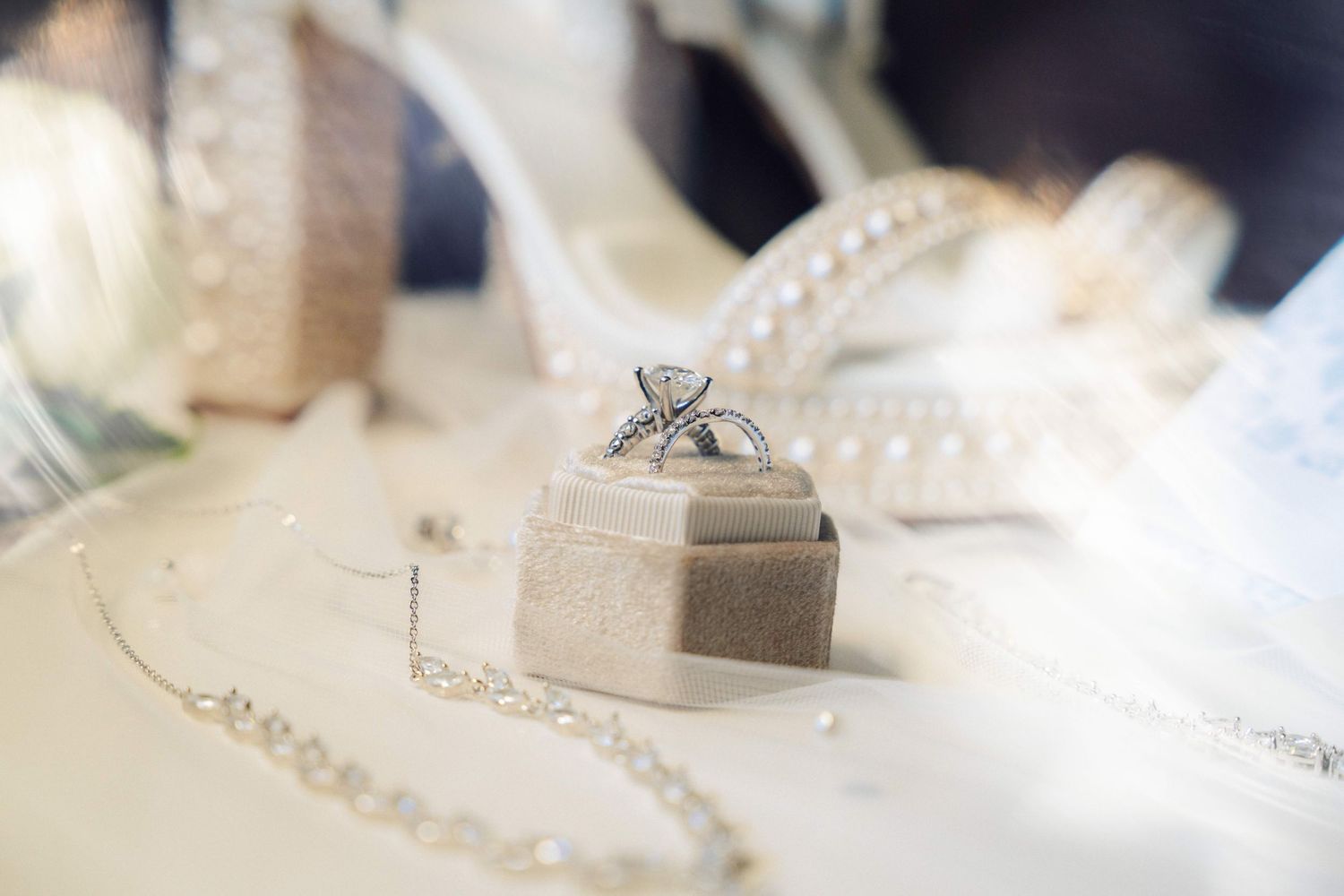 wedding ring detail show with her necklace on the foreground and the brides shoes in the background