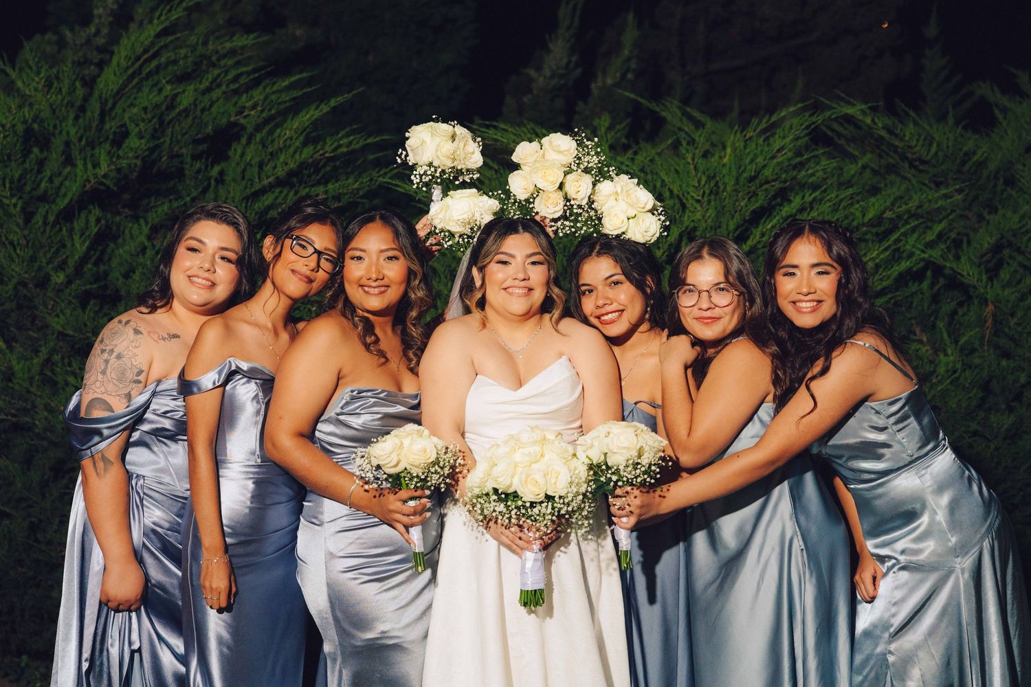 Bridal party all wearing blue and smiling for the camera with their flowers behind the bride