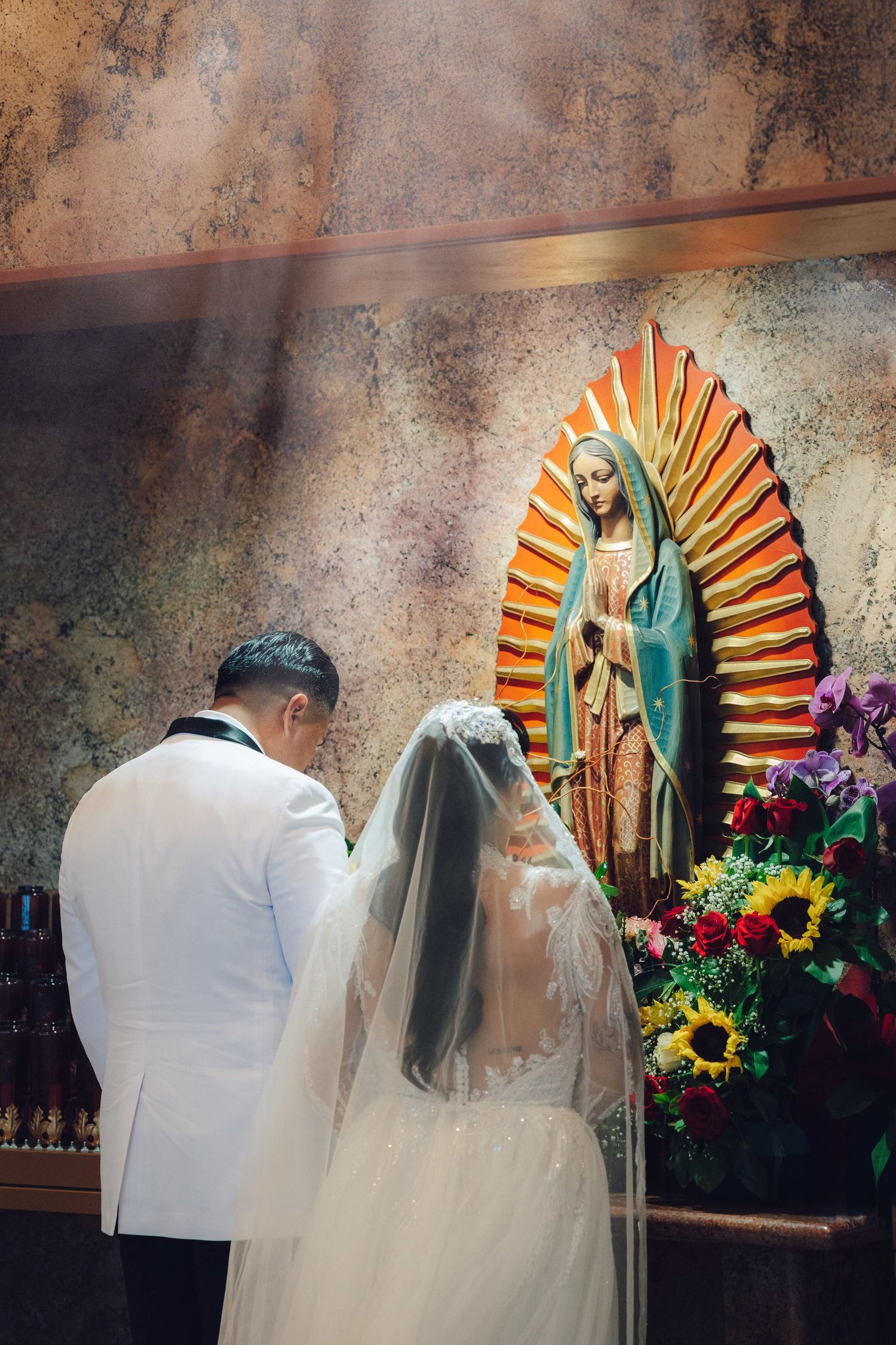 Bride and groom putting their head down in front of the virgin mary