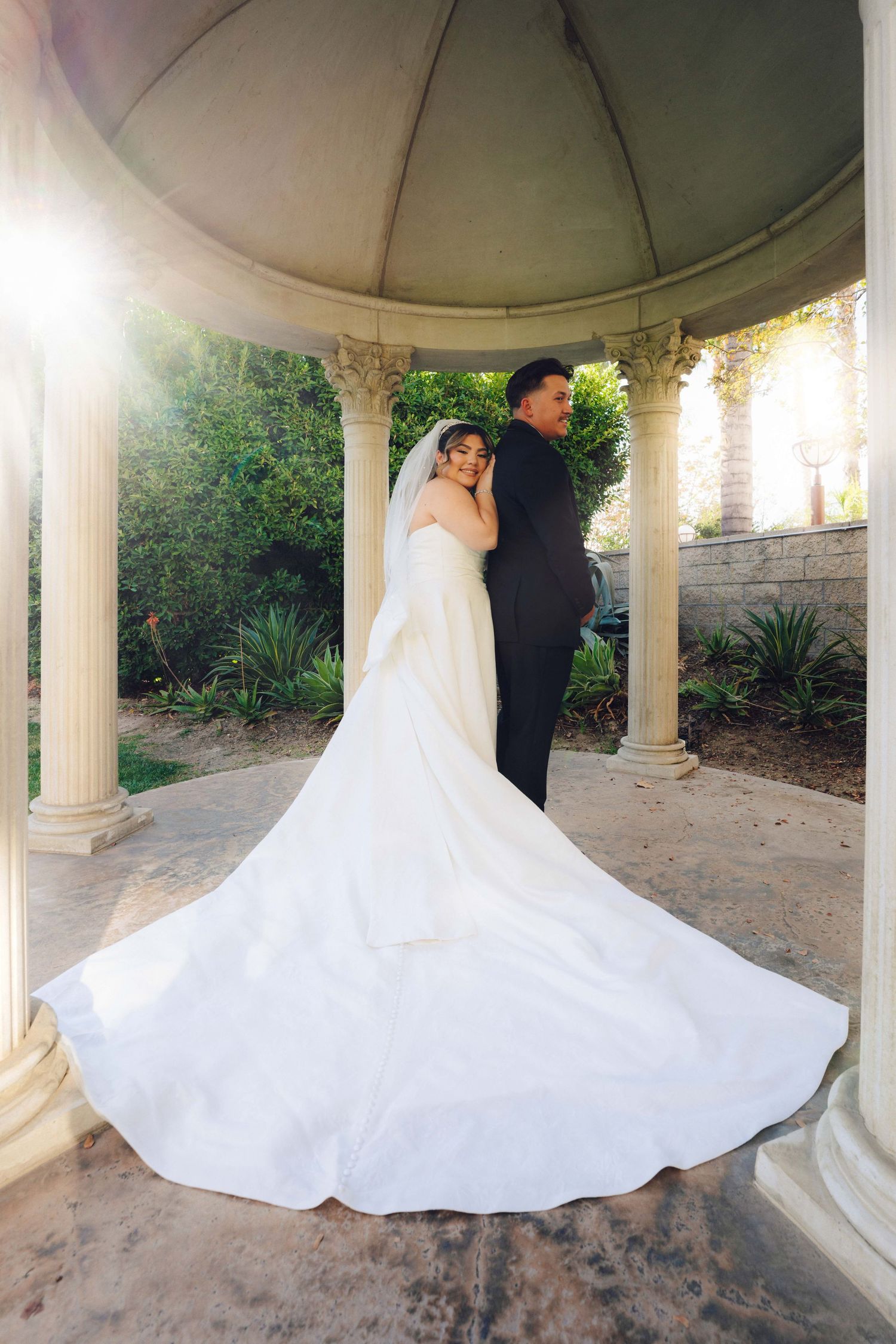Couple under gazebo at double tree hotel in rosemead. wedding dress tail is extended to show how long it is.
