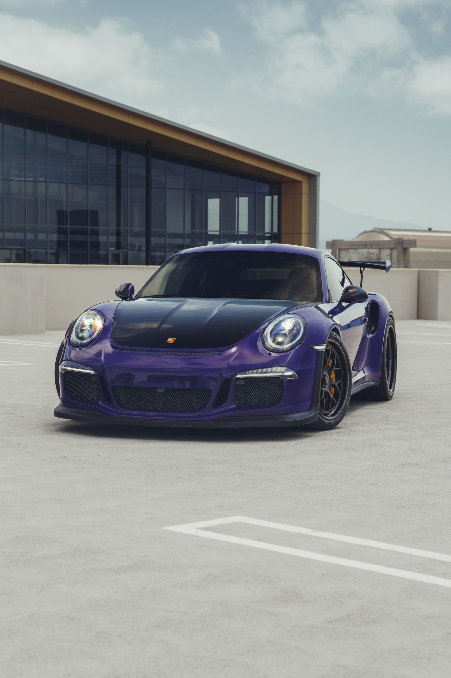 quarter shot of a porsche in a purple color with the wheel turned a little bit. You can see a art building behind the porsche.