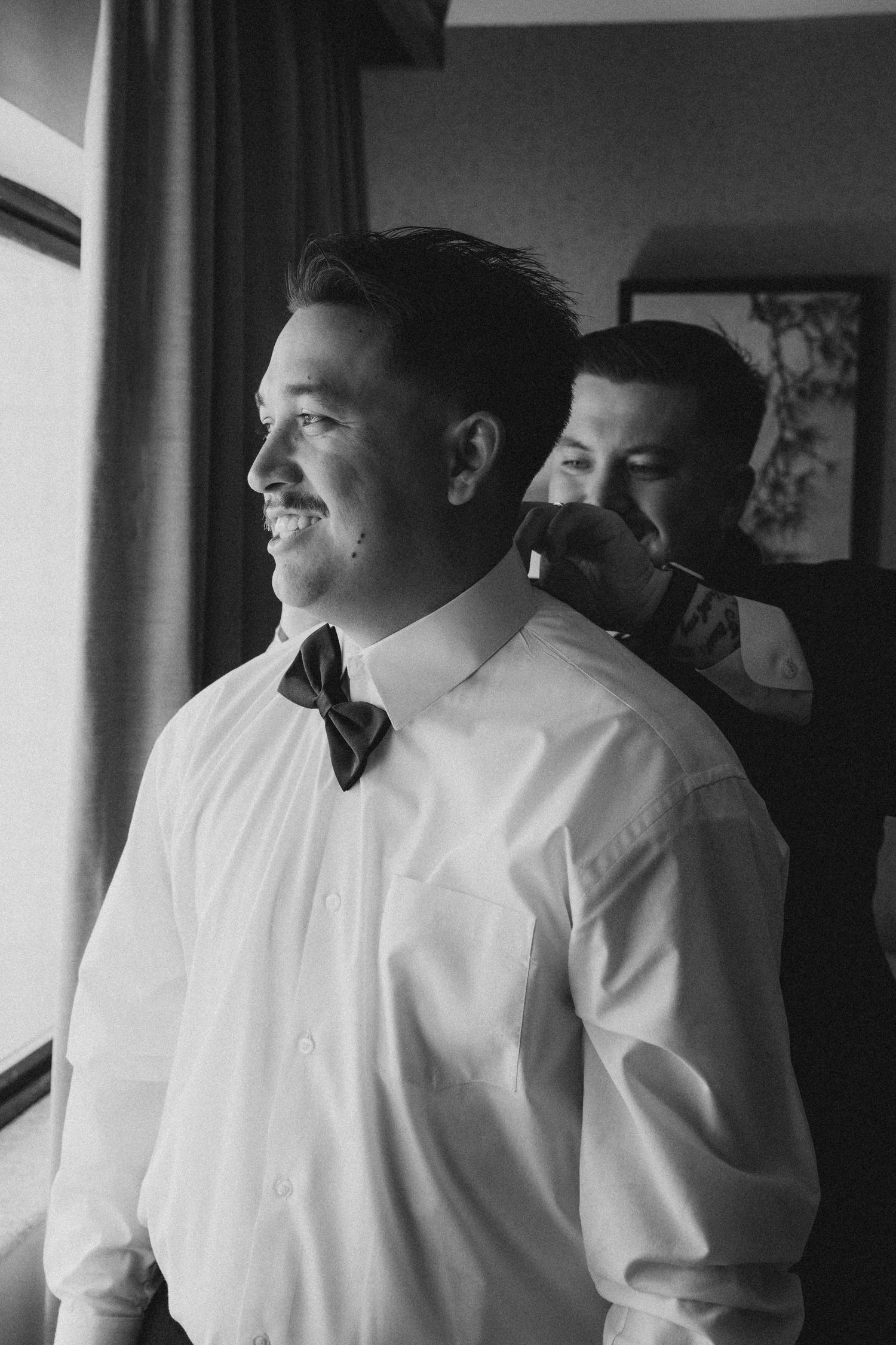 Groom getting his bowtie put on by his best man in the hotel room at the double tree in rosemead