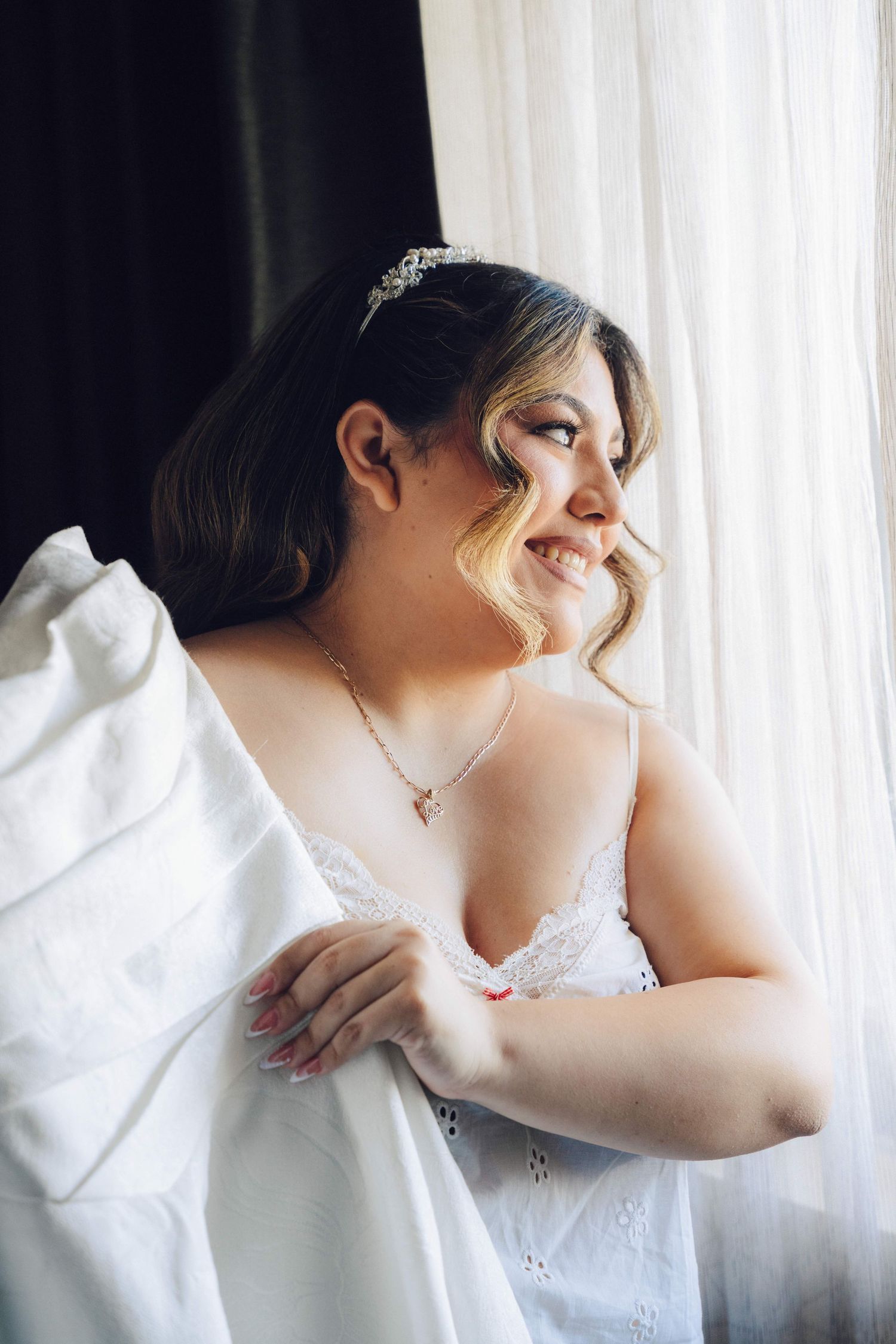 Bride looking out the window while holding her dress into the light