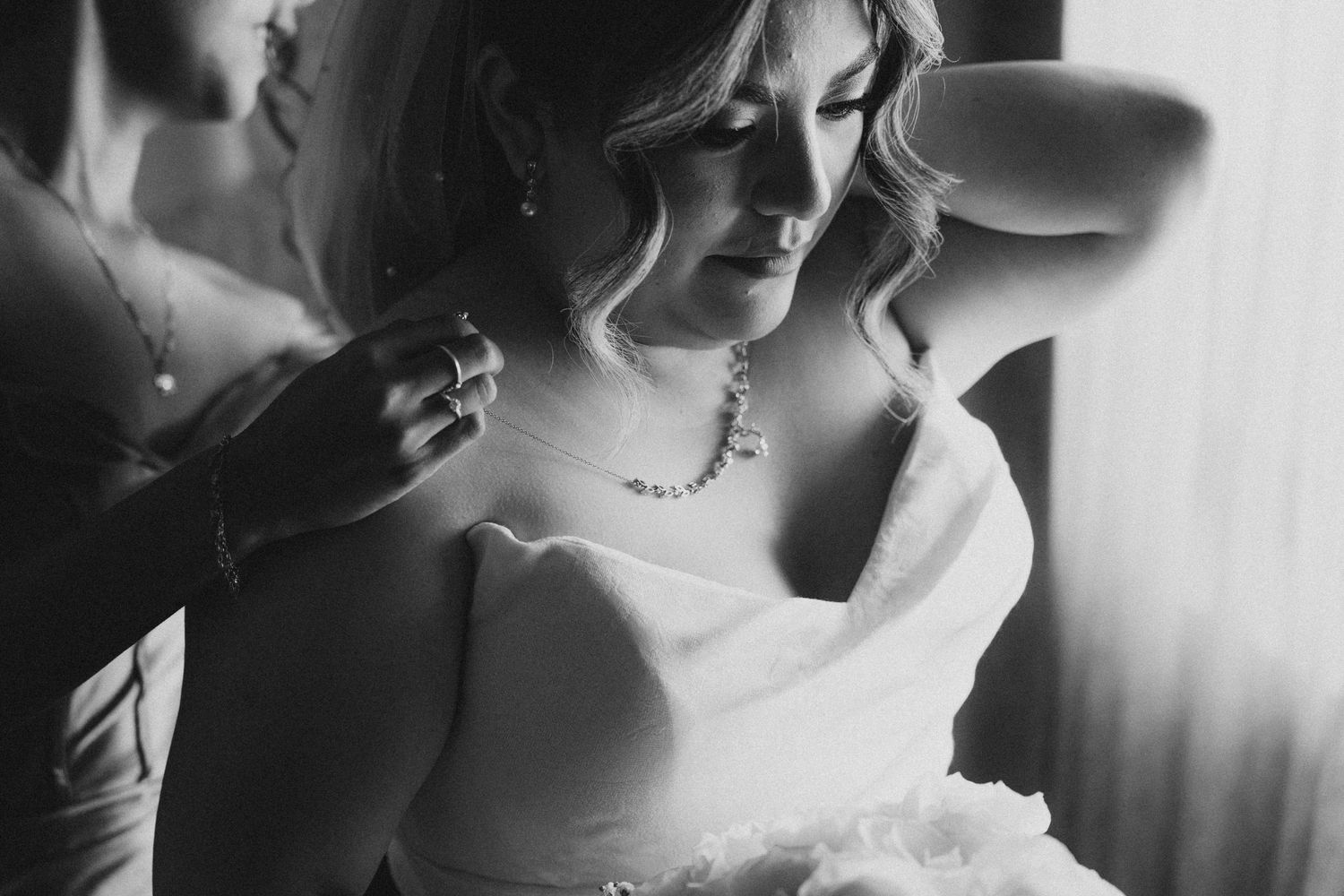 bridesmaid putting the necklace on the bride while she's getting ready