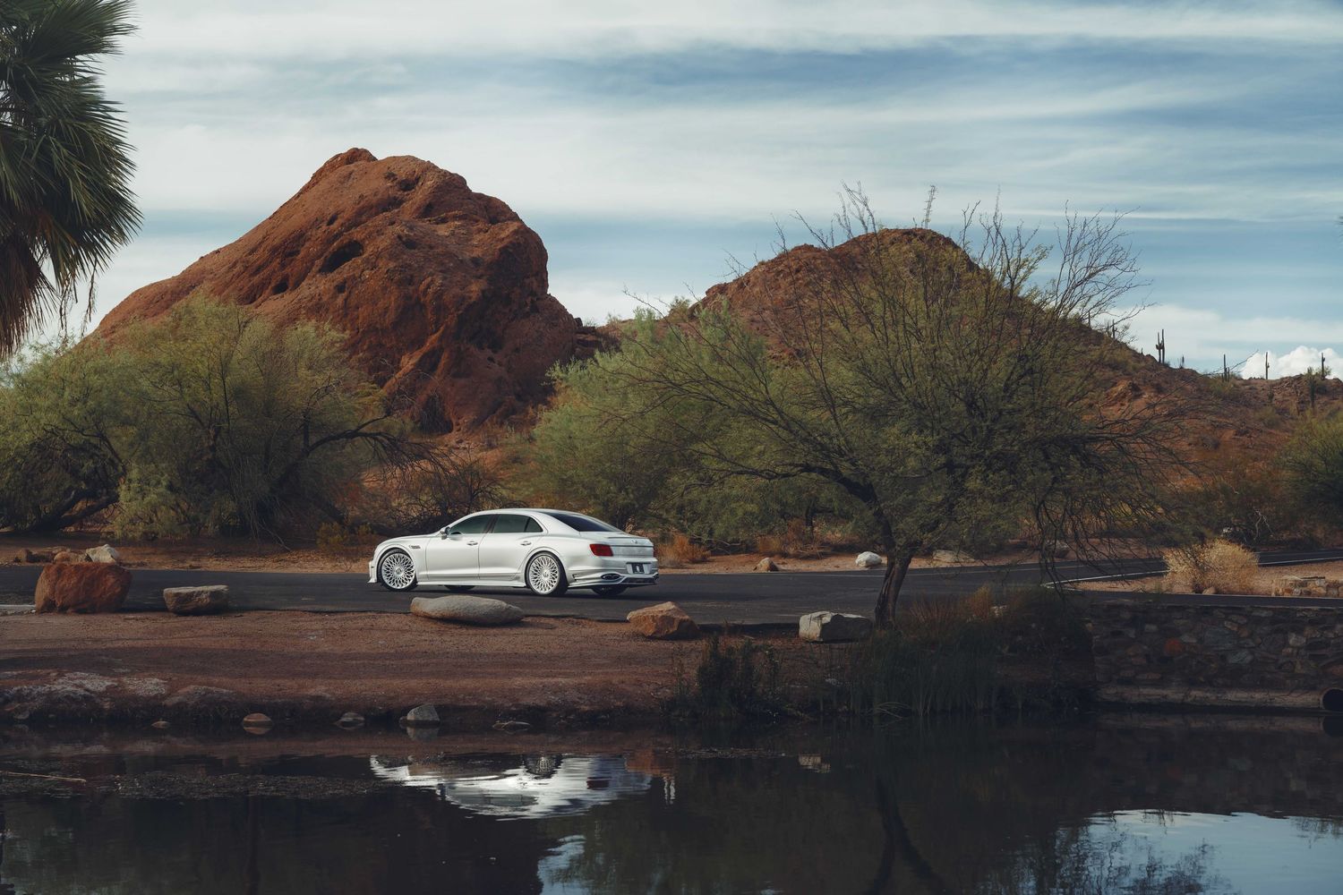 Bently flying spur parked next to some arizona red rock with a lake in the foreground