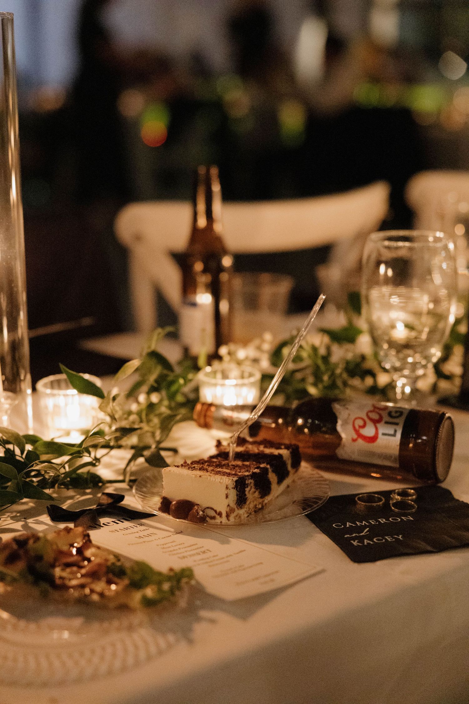 Romantic candlelit dinner table setting with wine bottles, greenery garlands and appetizer plates at an elegant reception.