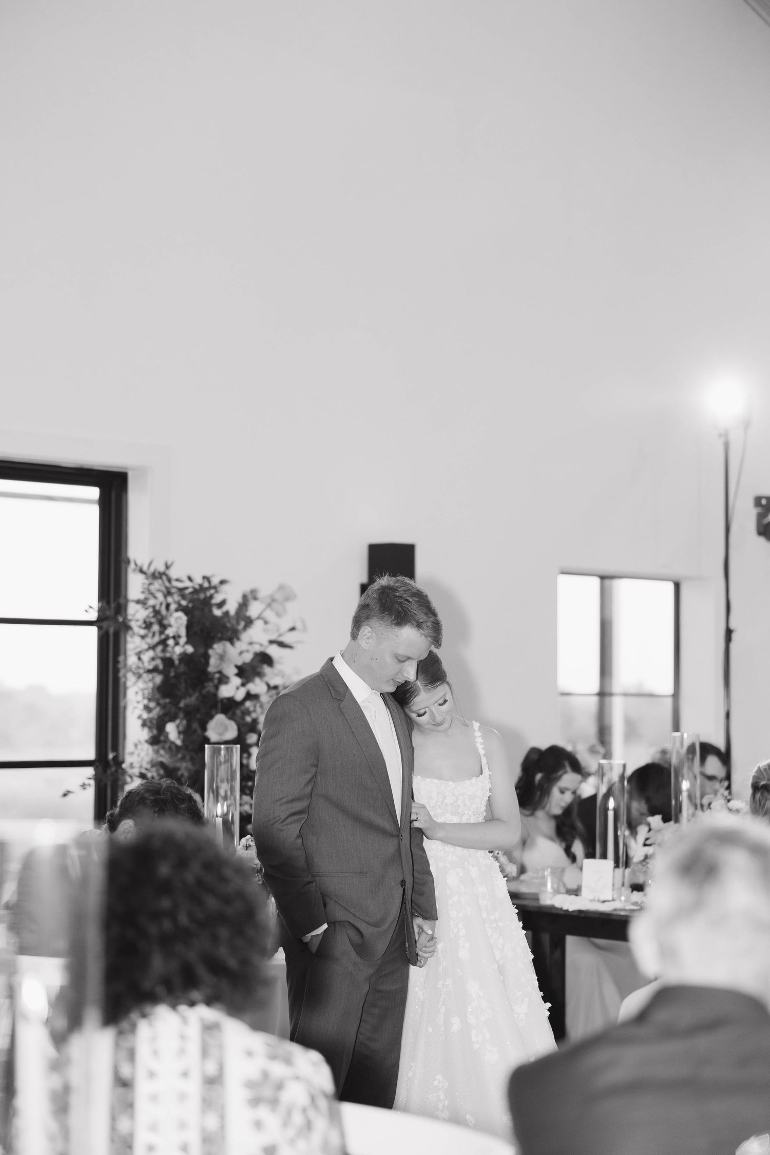 A tender moment captured in black and white at an elegant wedding reception with guests seated at tables.