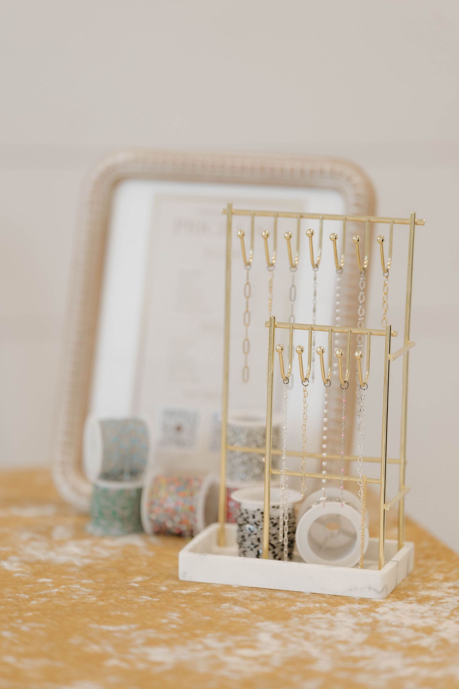A gold metal jewelry display stand with hooks sits on a velvet surface next to storage containers and a mirror.