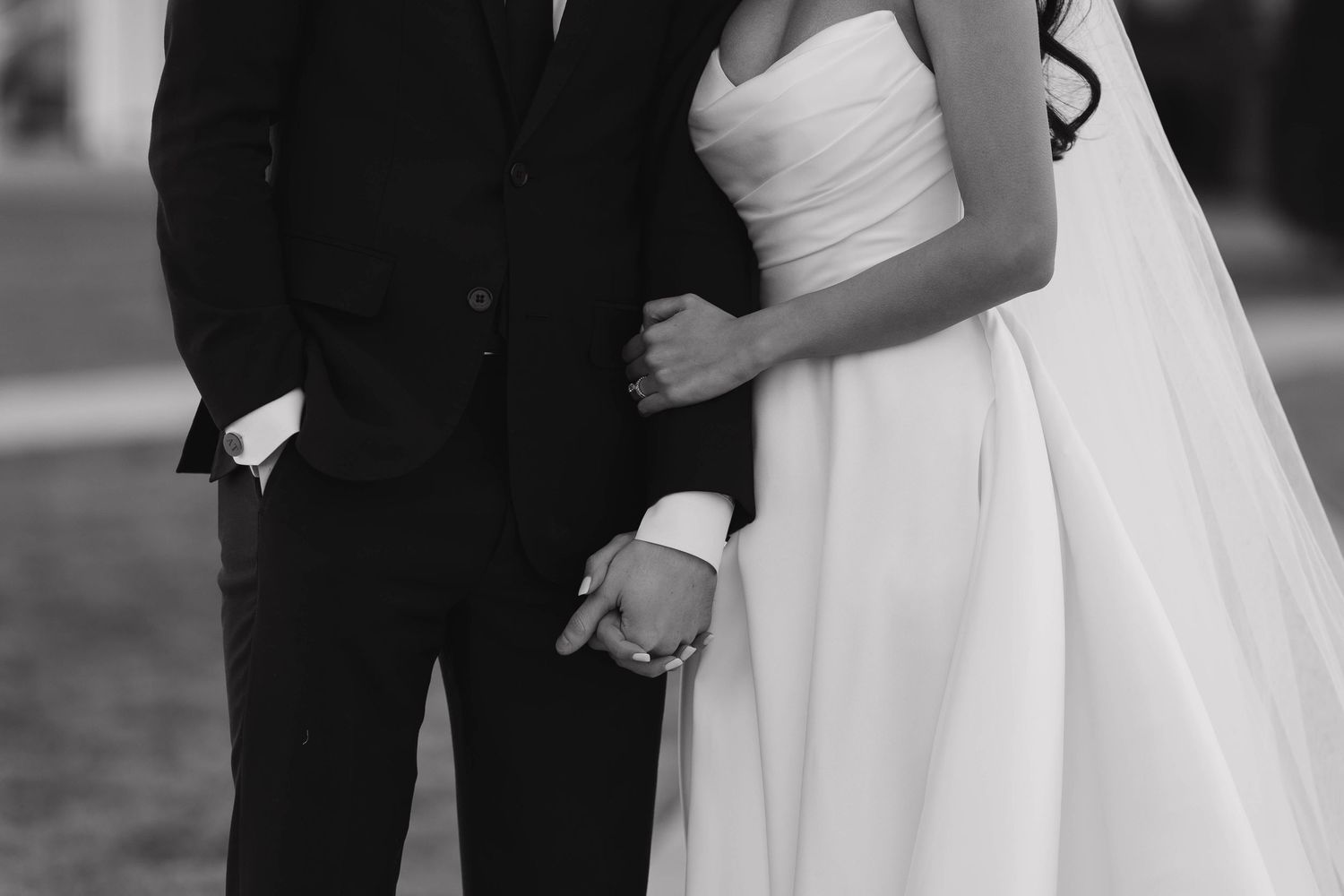 A close-up black and white photo shows a couple in formal wedding attire standing together outdoors.