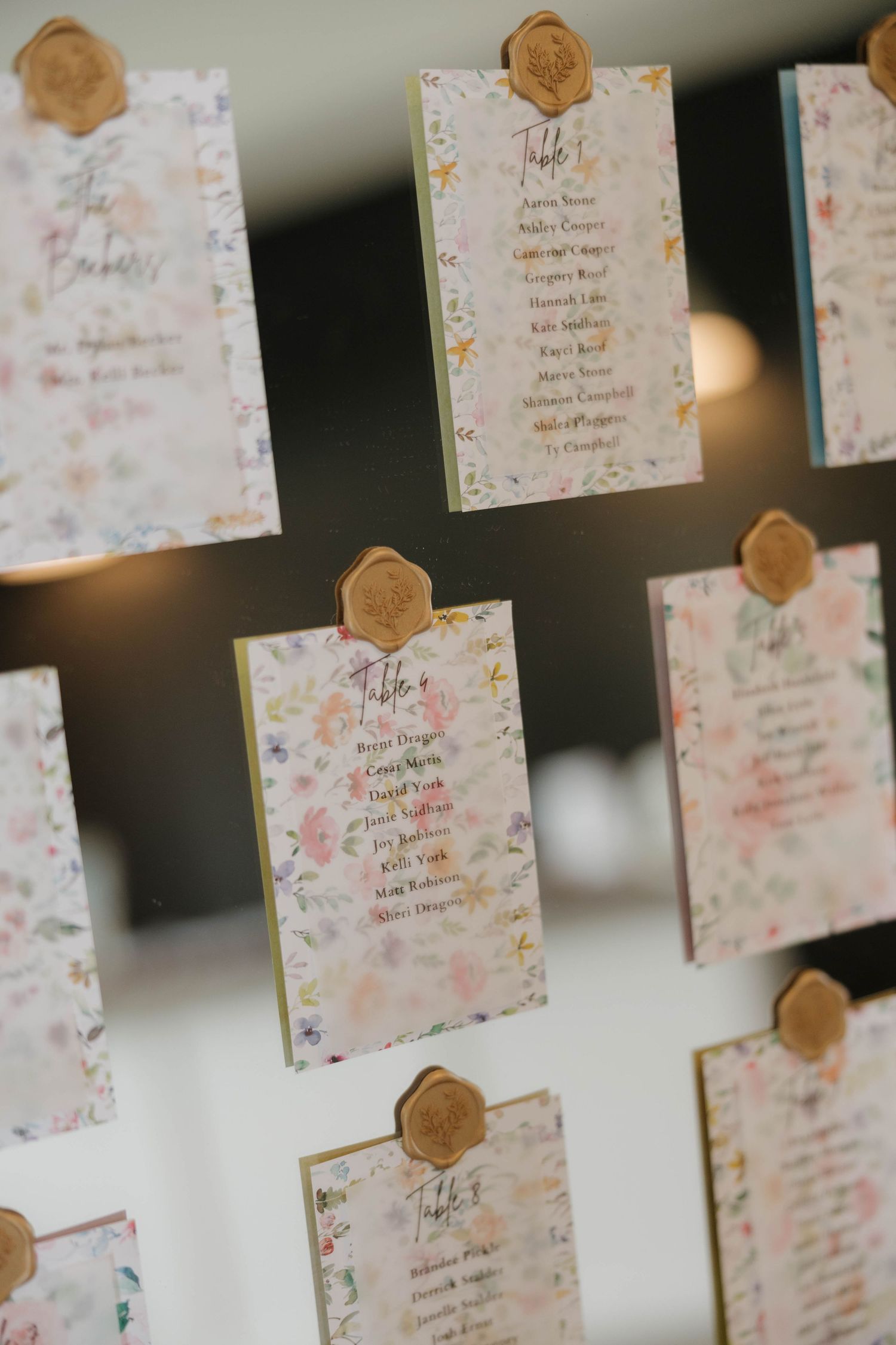 Wedding escort cards with delicate floral patterns and gold wax seals displayed in rows for seating arrangements.