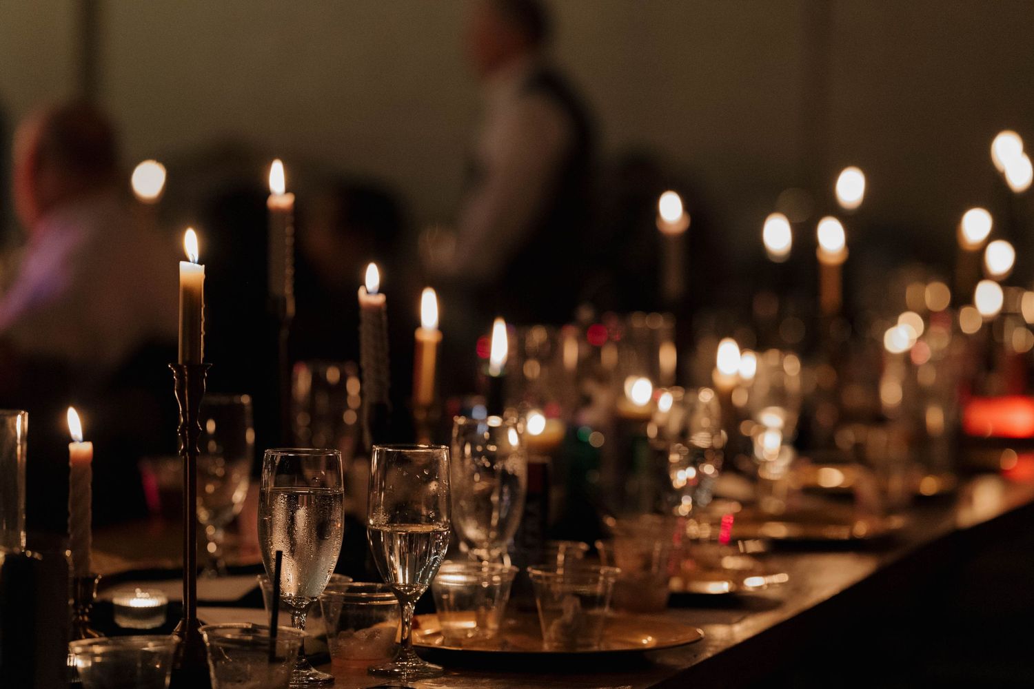Elegant dining table set with glowing candlesticks and wine glasses in a romantic dimly lit restaurant setting.