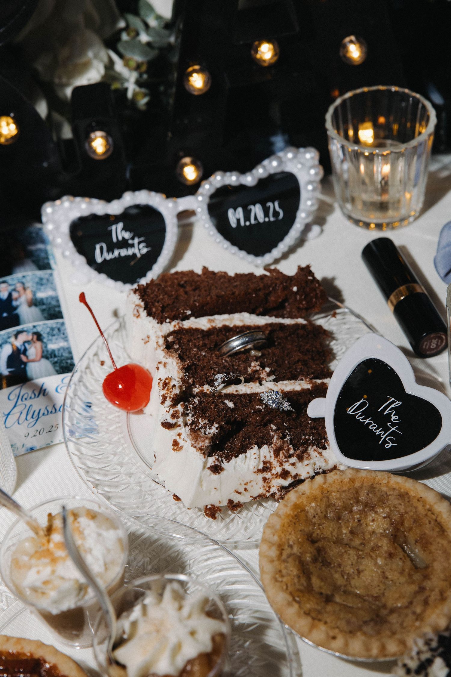 Chocolate cake slices and desserts arranged on plates with string lights and decorative labels at a festive gathering.