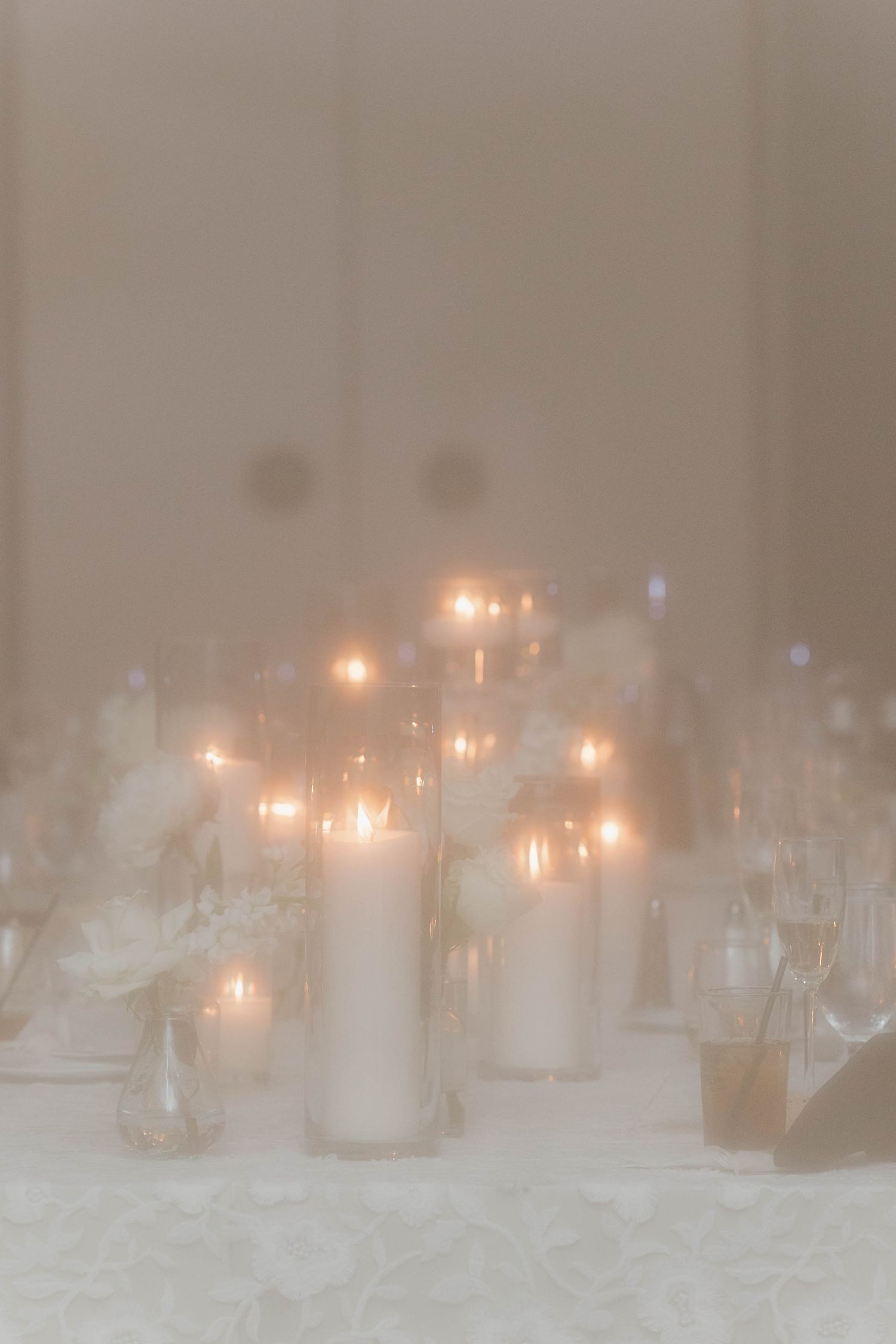 Multiple glowing candles in glass jars create a romantic, soft-lit ambiance on a white surface through misty lighting.