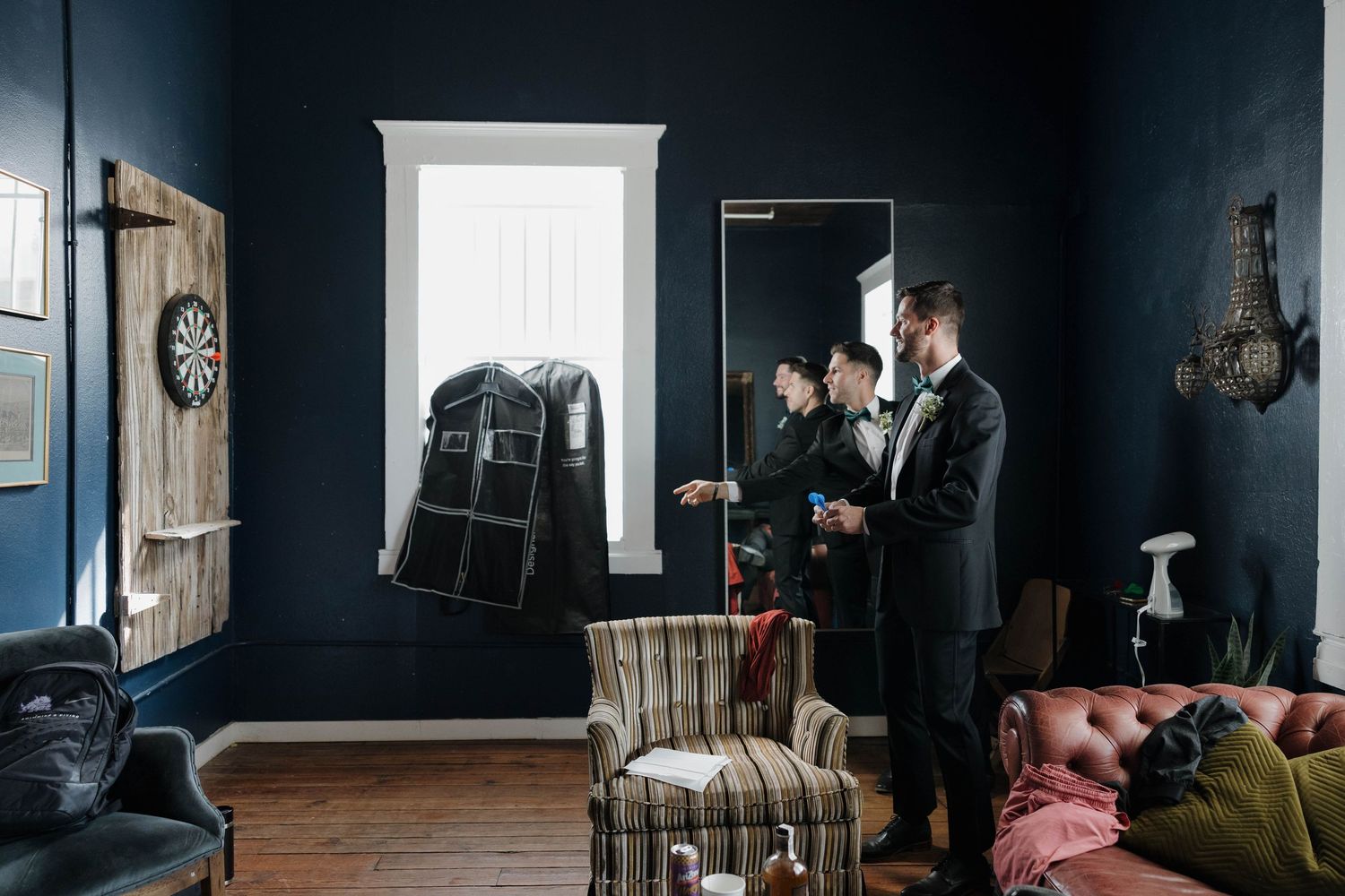 Men in dark suits getting ready in a moody blue room with vintage furniture and white trim details.