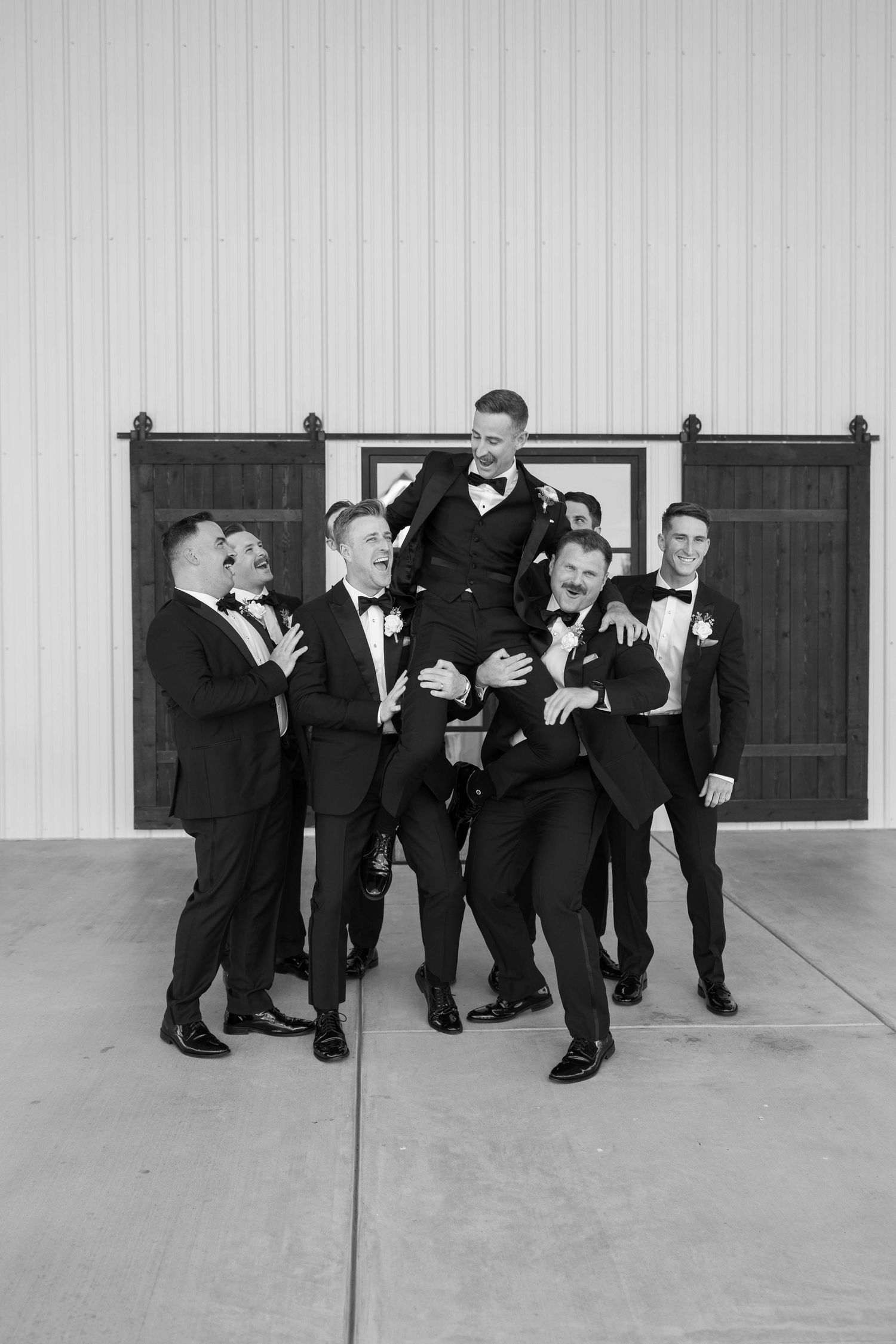 A group of groomsmen in black suits playfully leap and pose in the air for a creative wedding photo sequence.