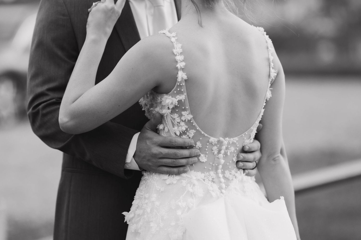 Couple embraces in elegant wedding pose while dancing outdoors in black and white formal attire.