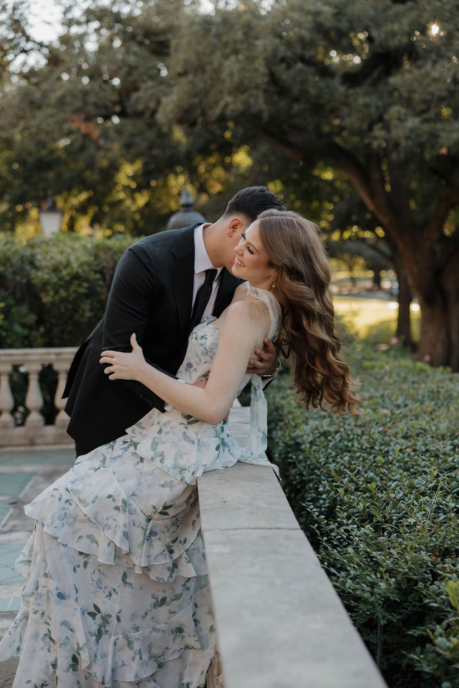 Romantic couple sharing an intimate moment on stone balustrade in garden setting.