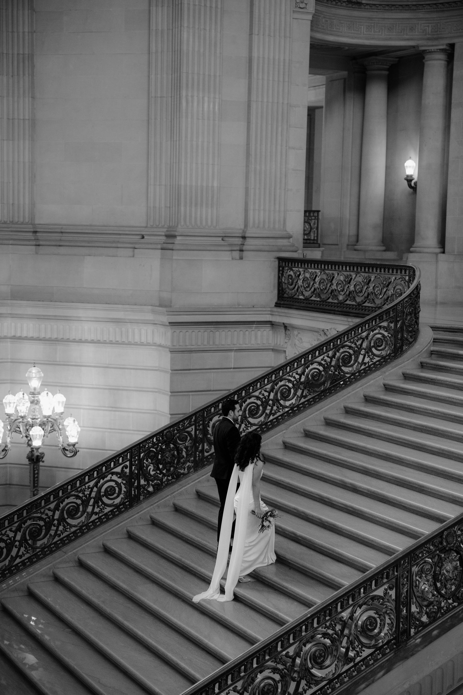 A black and white photograph of an elegant grand staircase with ornate wrought iron railings in a classical building.