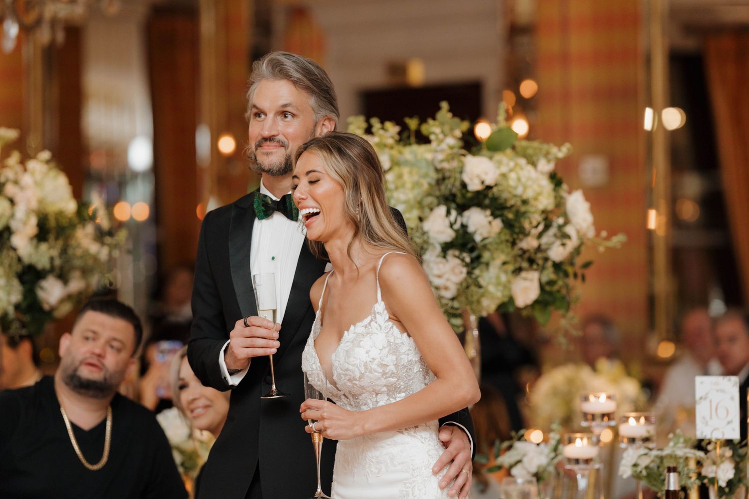 Wedding reception scene with elegant floral centerpieces and guests celebrating at decorated tables.
