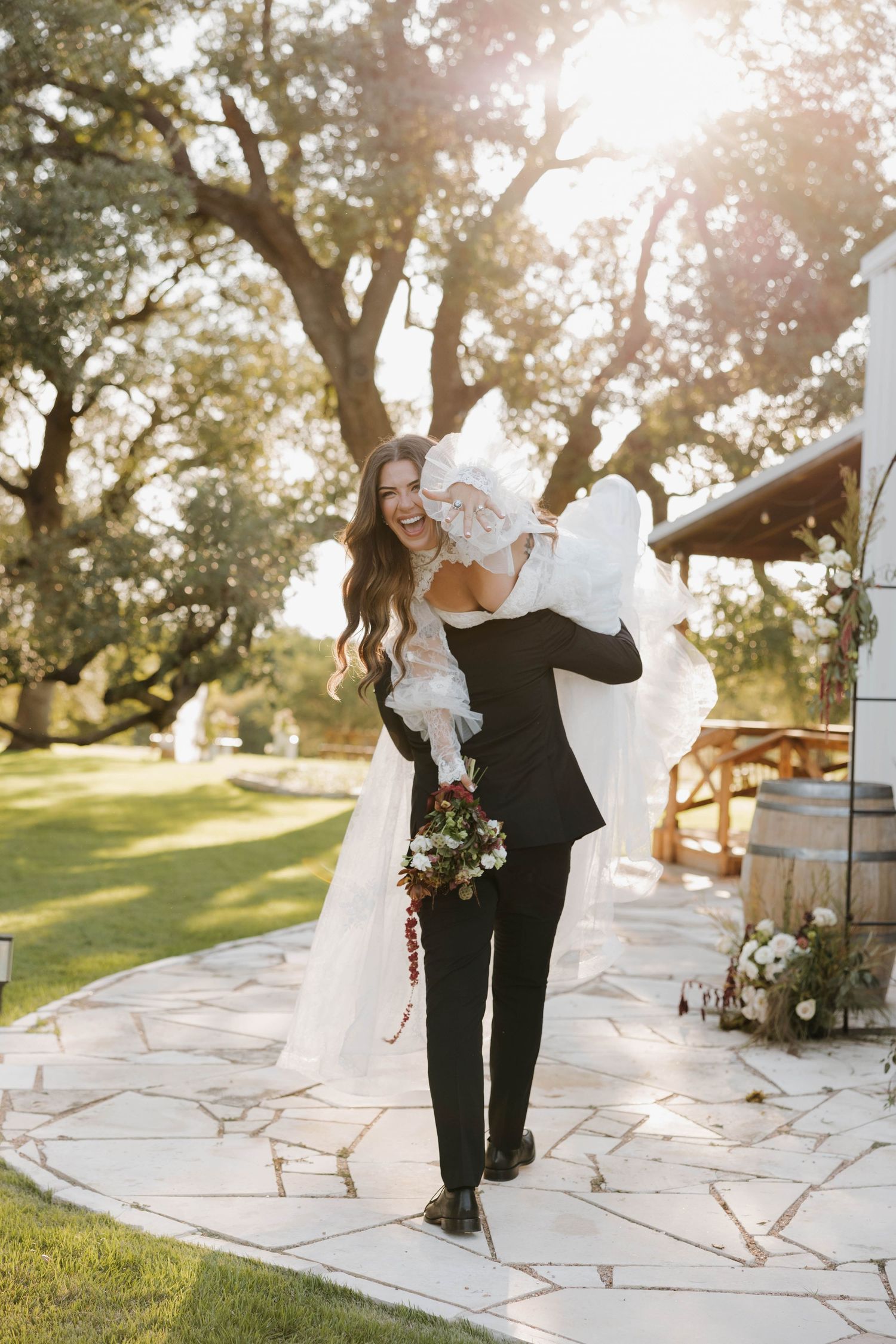 A romantic couple dancing together on a stone patio at sunset with oak trees in the background.