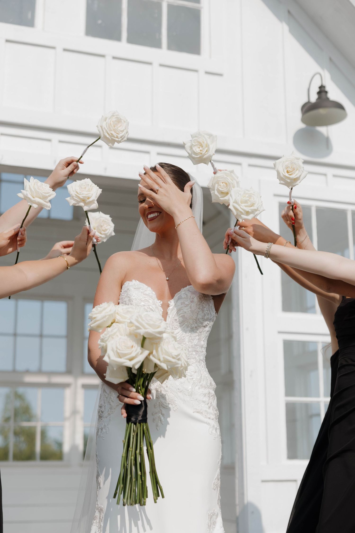 Joyful wedding moment with white roses held up by friends to celebrate the bride in a lace strapless gown.