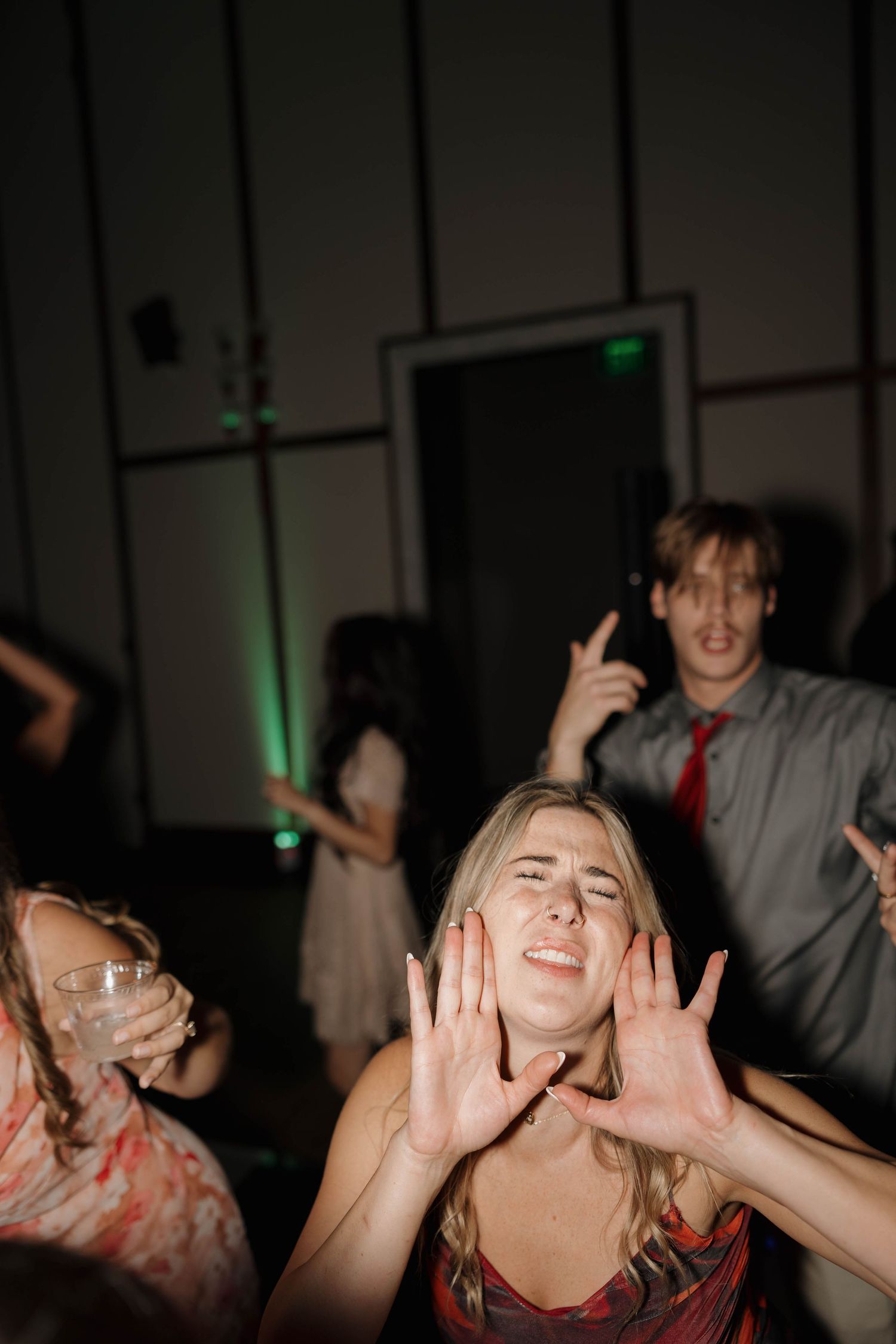People enjoying themselves and dancing energetically at a party with green lighting in the background.