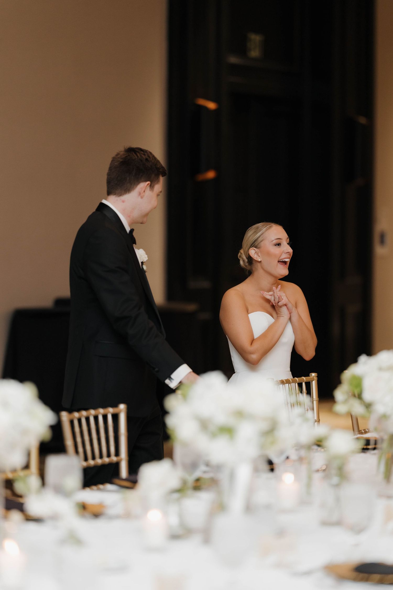 An elegant wedding reception table decorated with white floral centerpieces and candles as newlyweds share a moment.