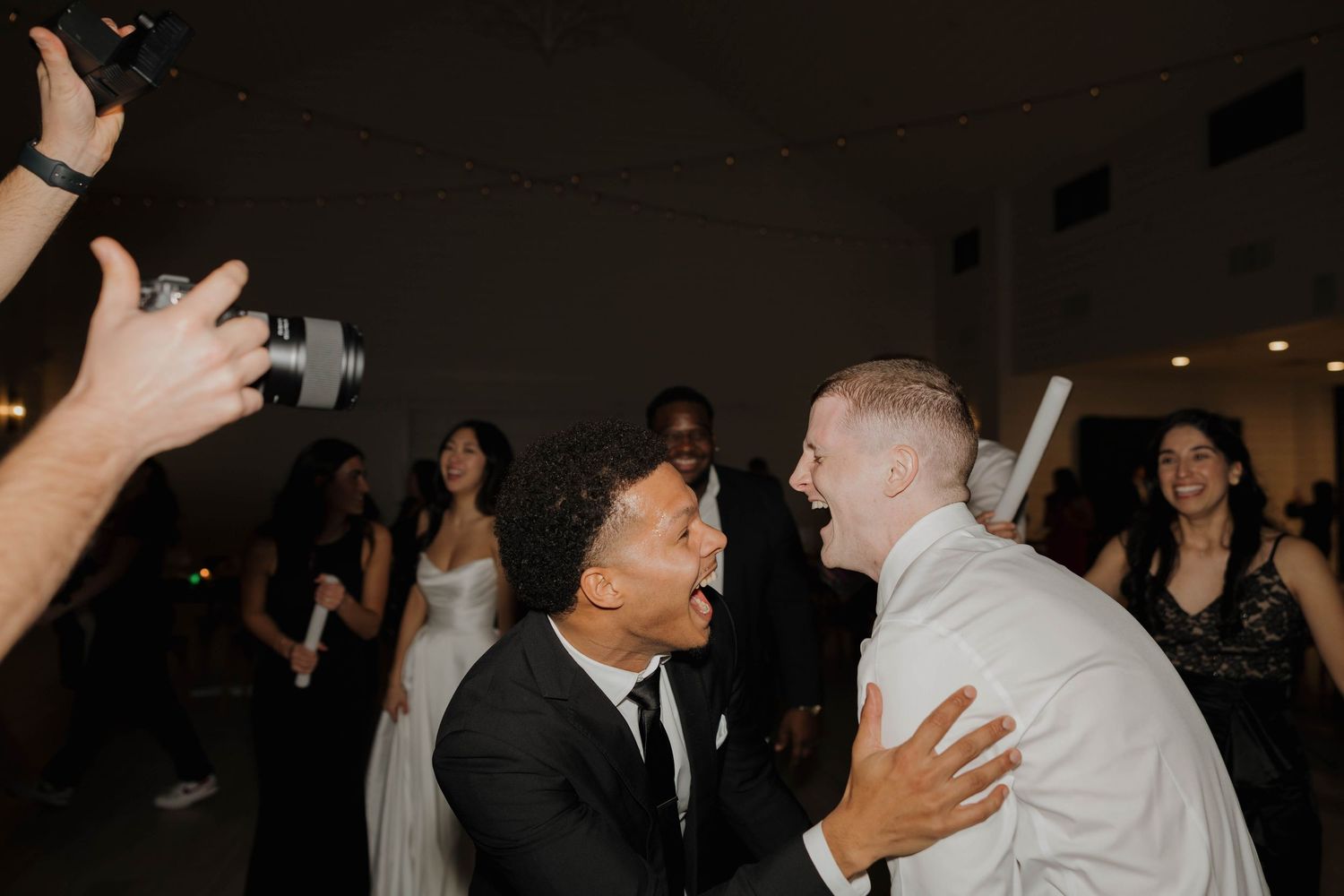 Two people share an energetic moment on the dance floor while wedding guests look on during a reception celebration.