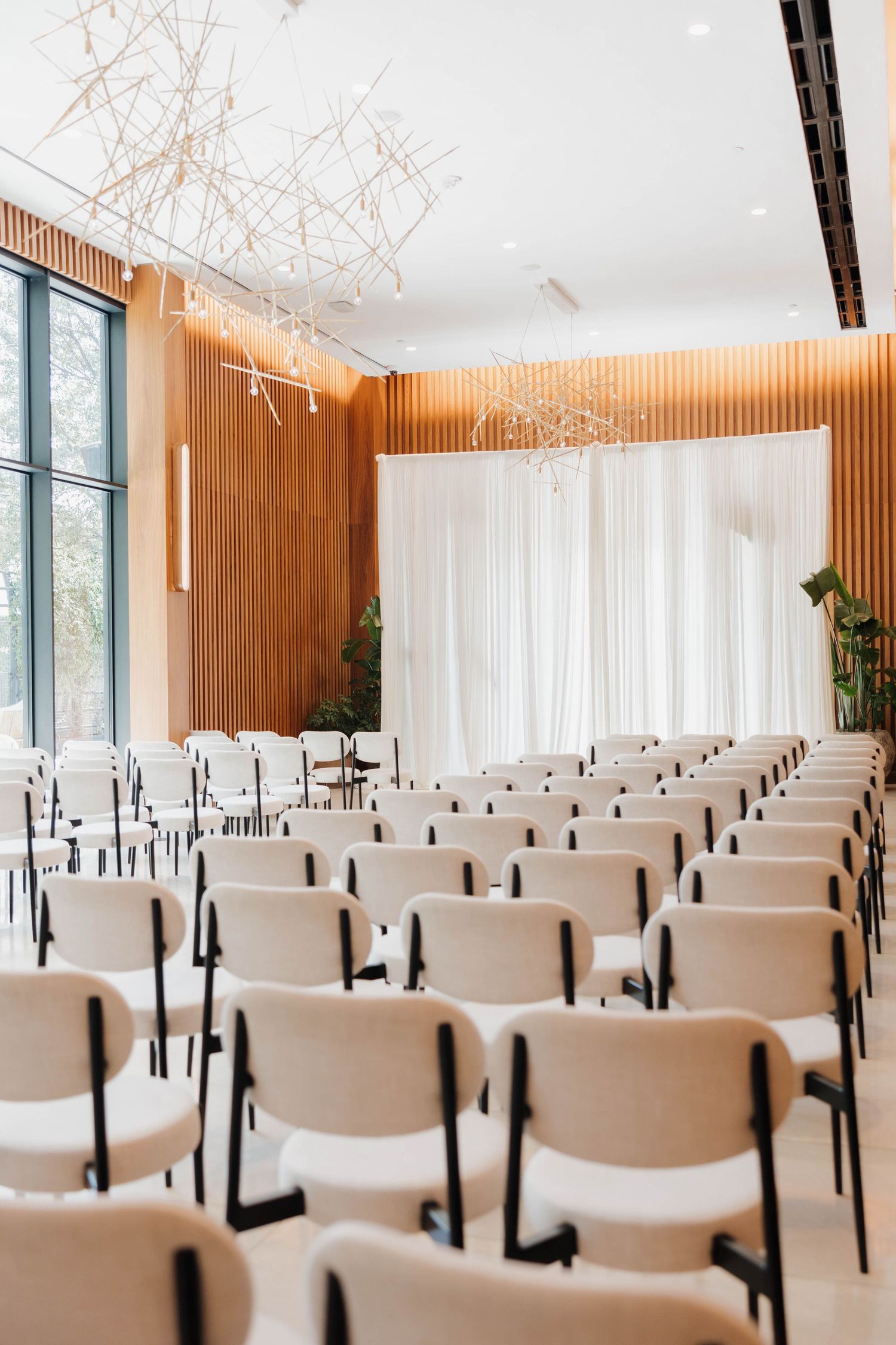 Modern event space with wooden slat walls, white chairs in rows, and contemporary geometric lighting fixtures.