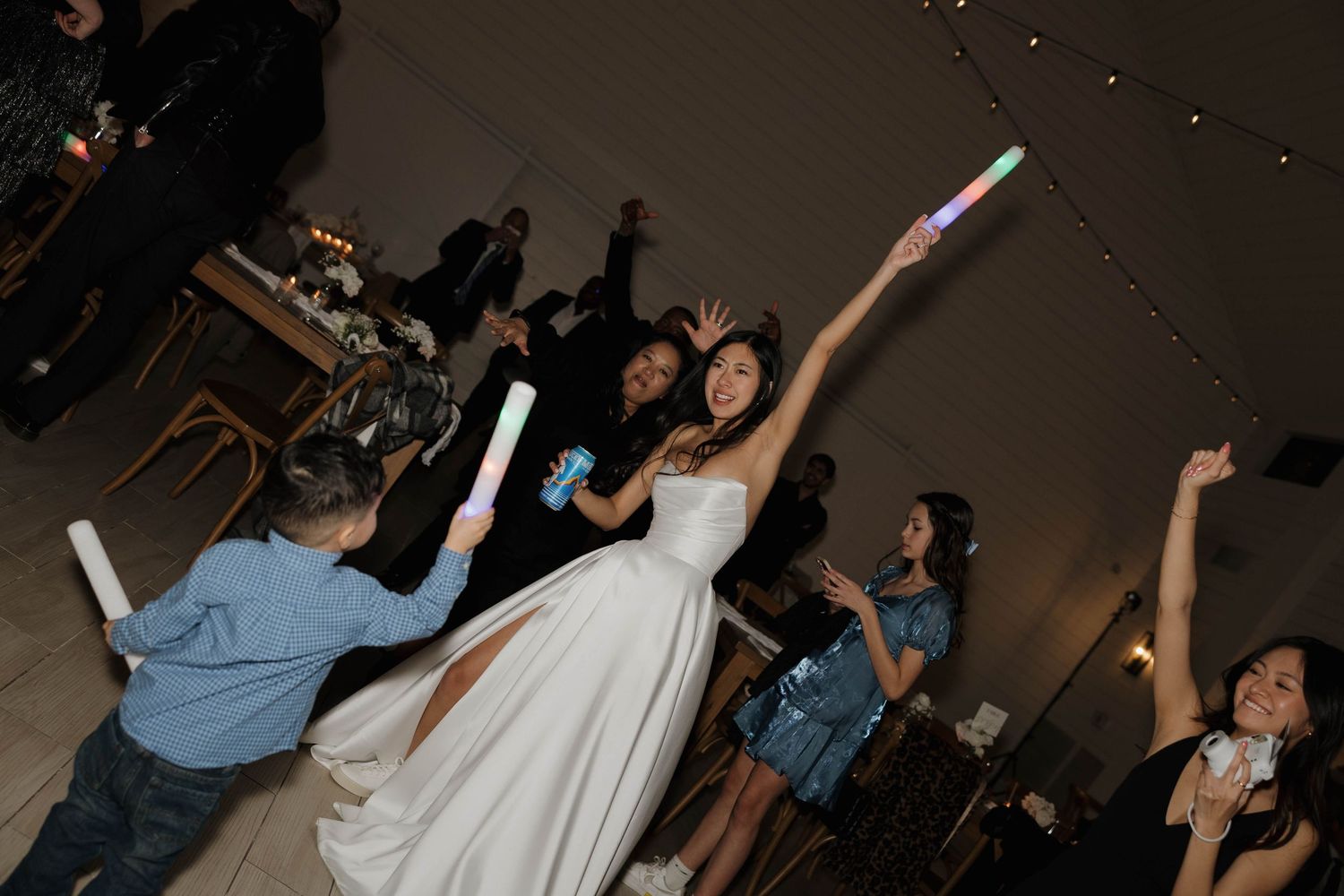 Wedding guests and newlyweds dancing with glowing light sticks on a dark dance floor during the reception celebration.