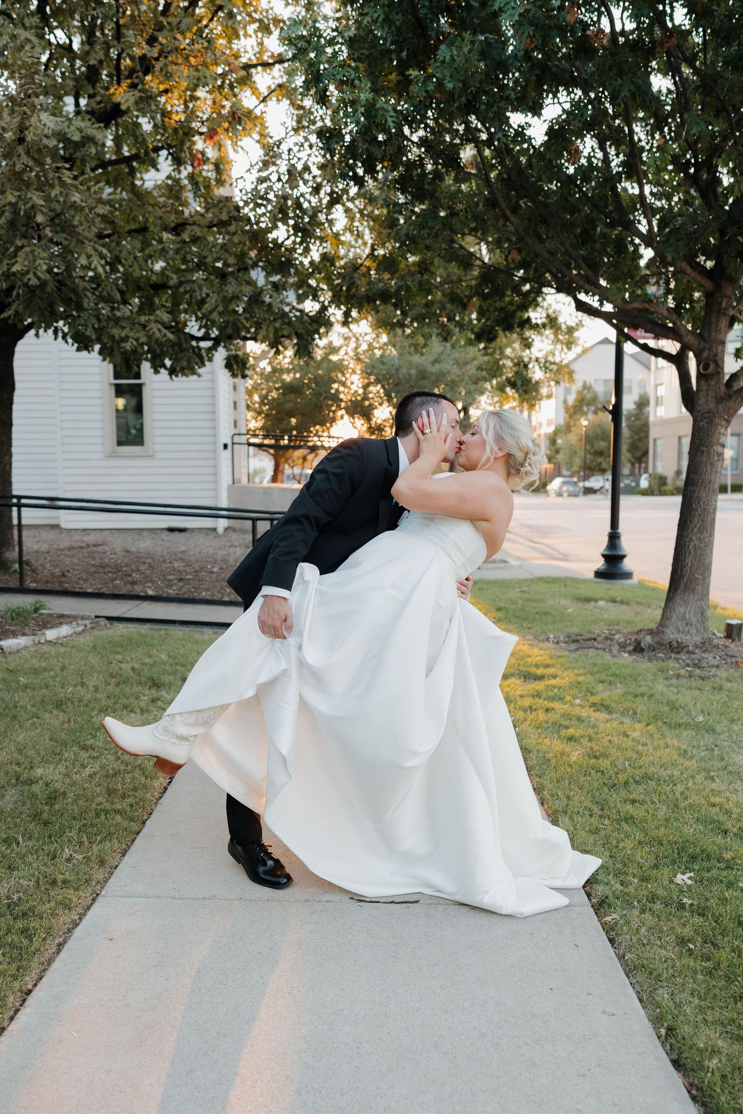 Romantic wedding dip pose on a sidewalk at sunset with trees in background.
