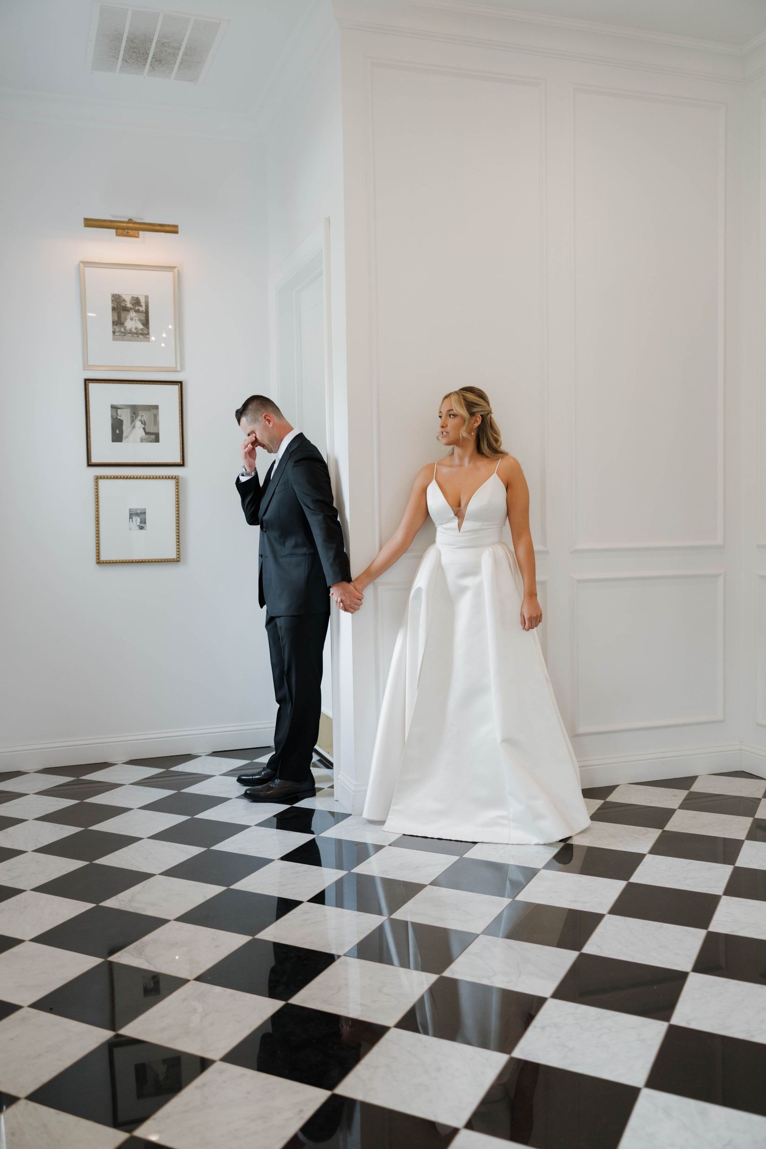 A couple shares an intimate first look moment on a black and white checkered floor in an elegant white room.