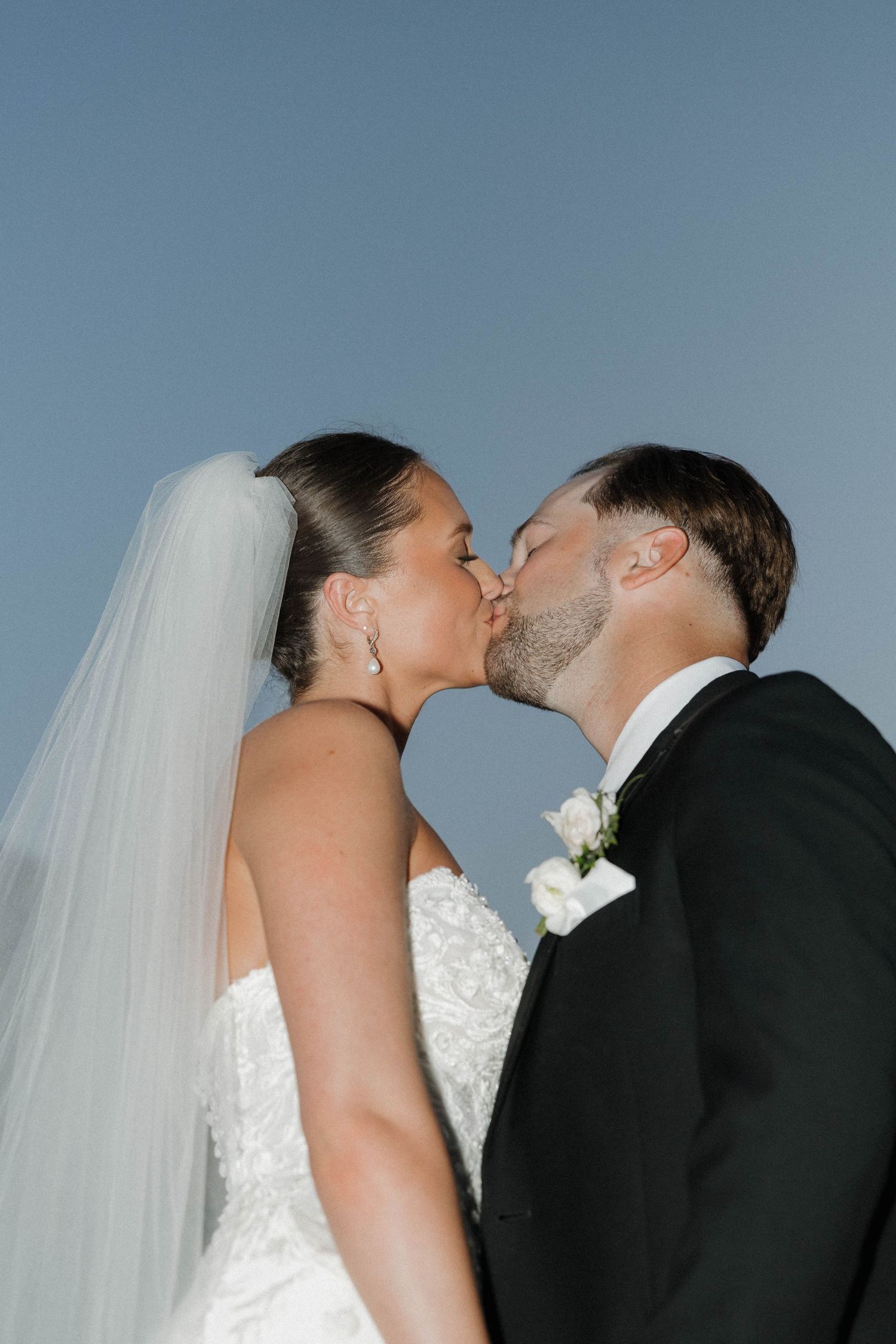 A tender kiss between newlyweds during their wedding ceremony, with the bride in white and groom in classic black.