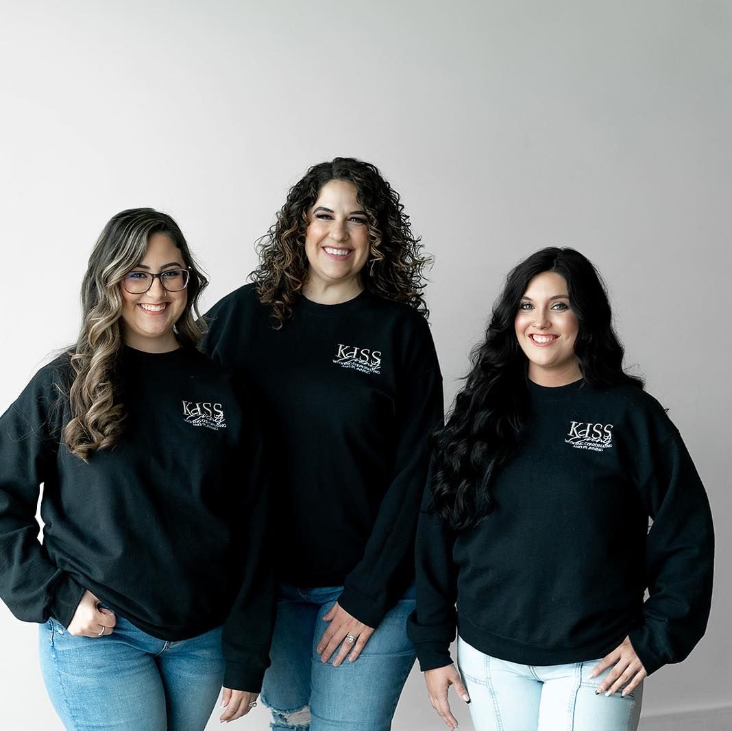 Three team members wearing matching black sweatshirts pose against white background.