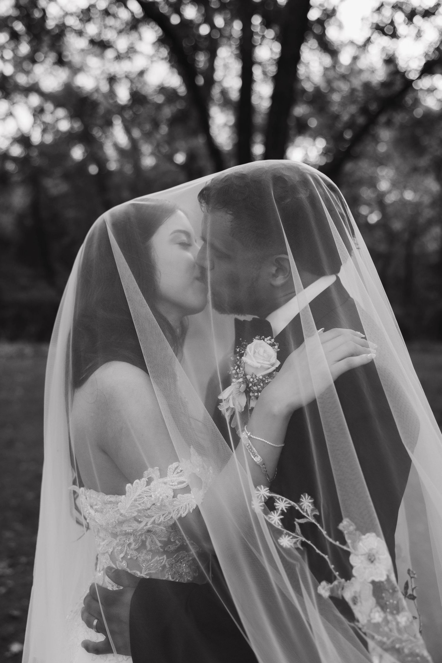 Intimate black and white wedding portrait through delicate veil outdoors.