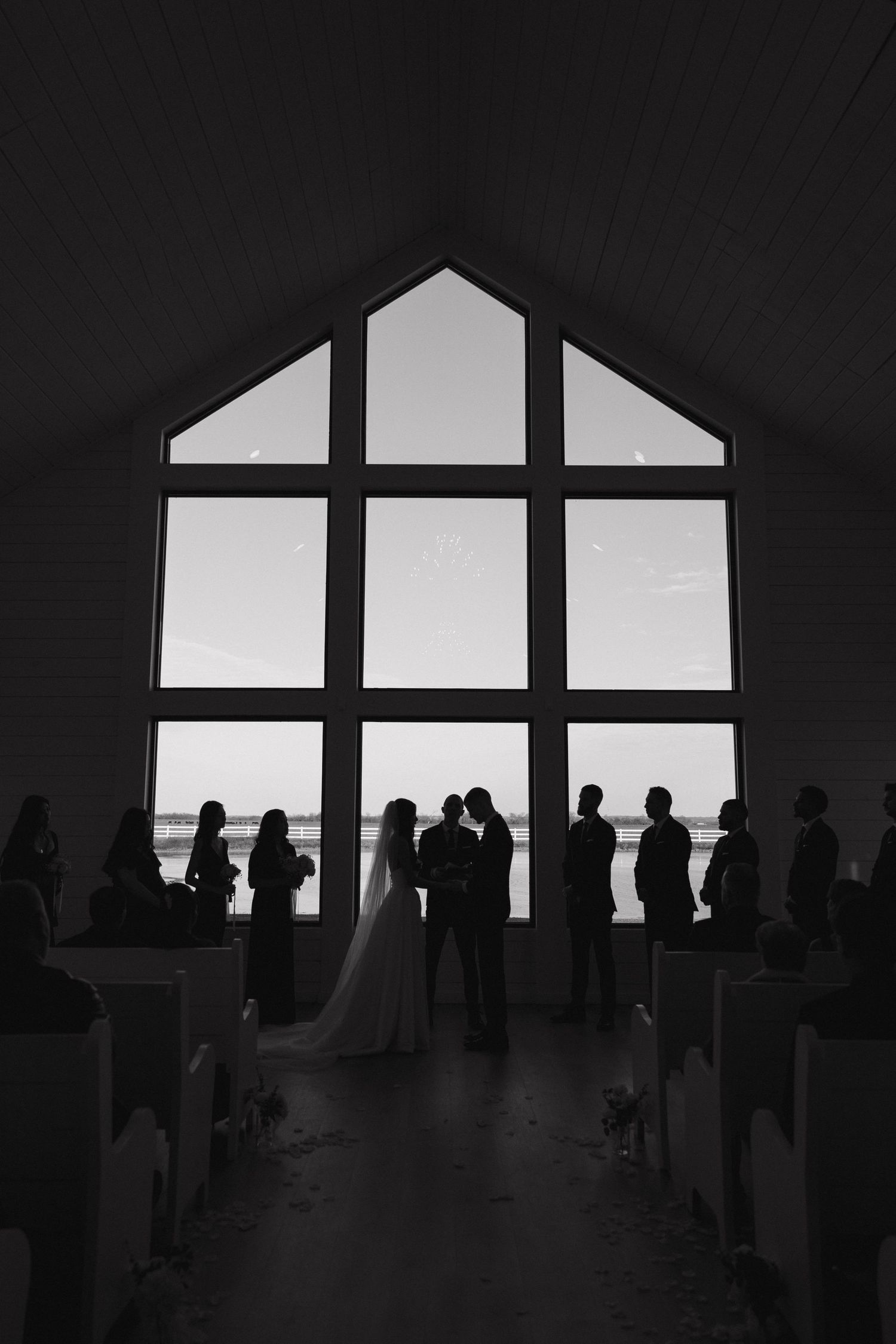 Silhouettes of visitors stand against a large geometric window overlooking a sunset in a modern art museum gallery.