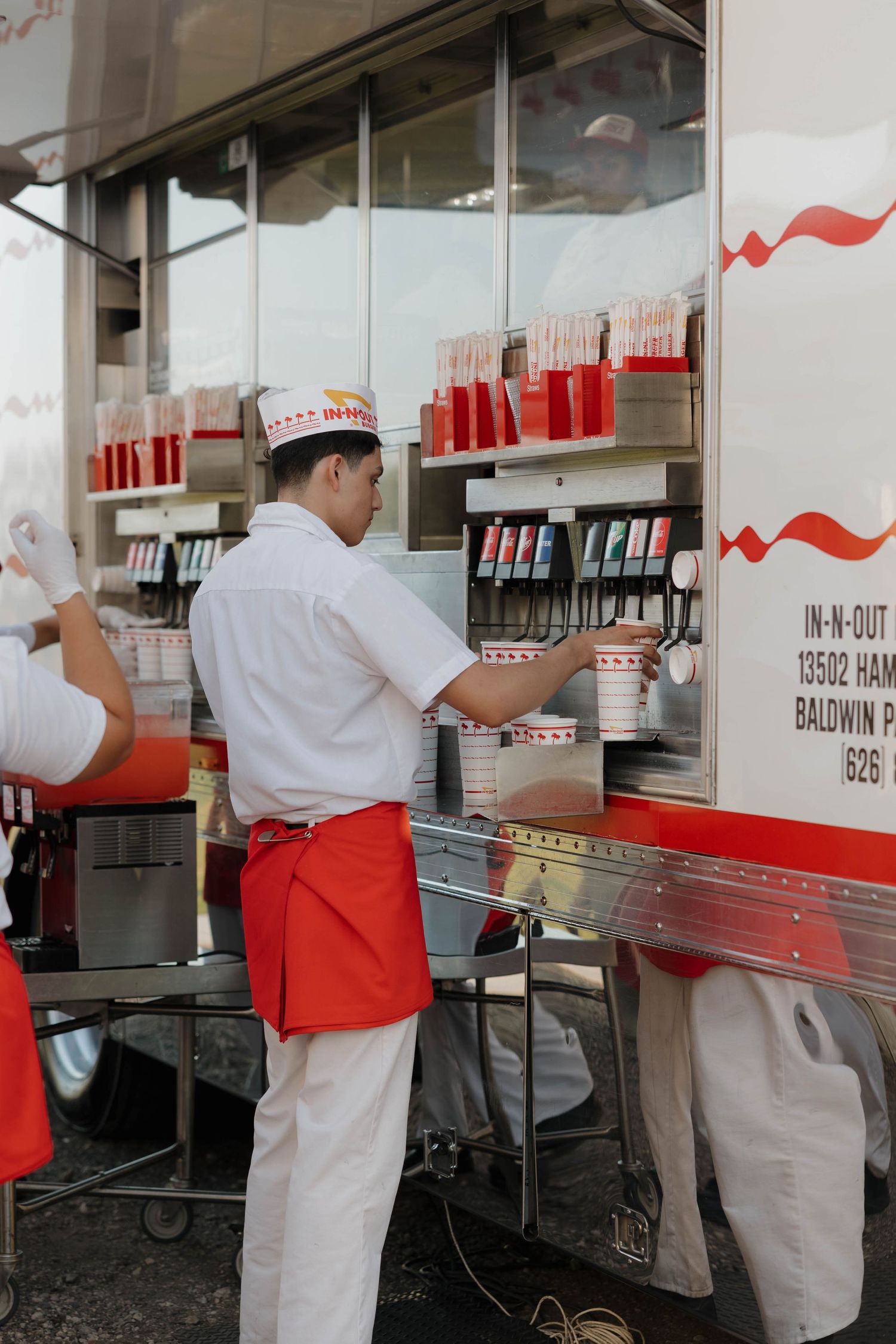 In-N-Out burger employee in red and white uniform prepares food at service counter.