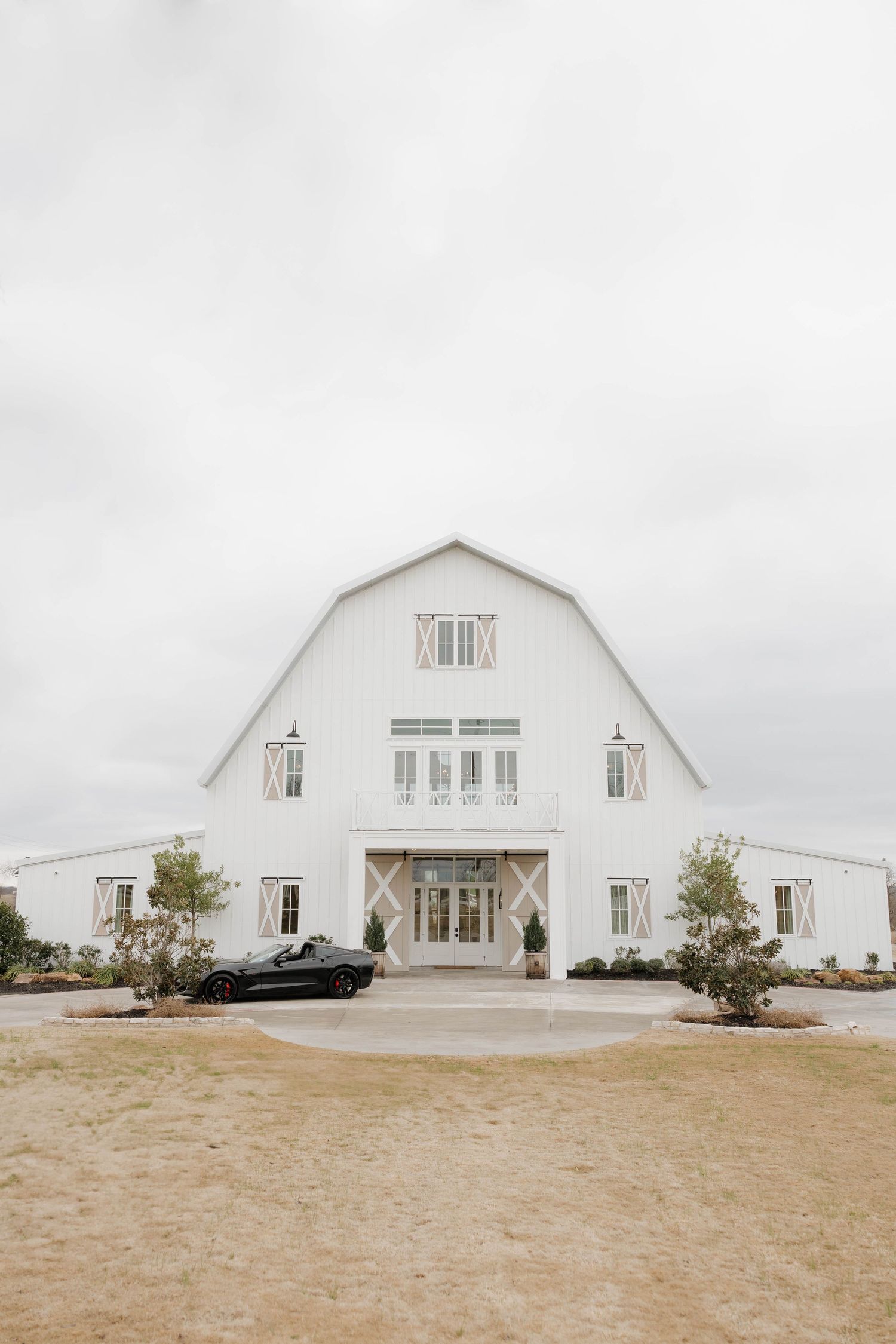 White barn-style wedding venue with gambrel roof and grand entrance against an overcast sky.