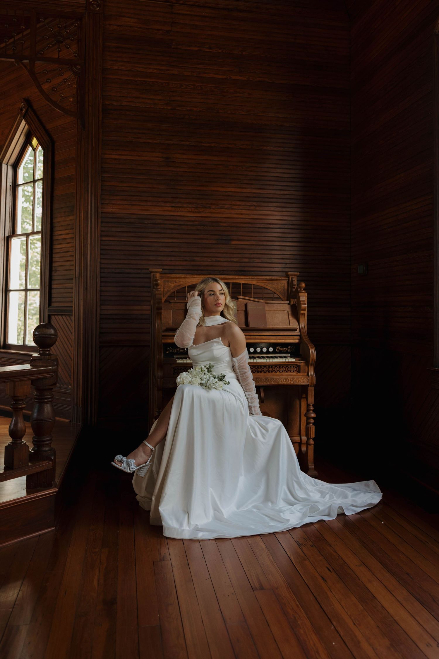 A white wedding dress displayed elegantly on a wooden piano in a rustic room with natural light streaming through windows.