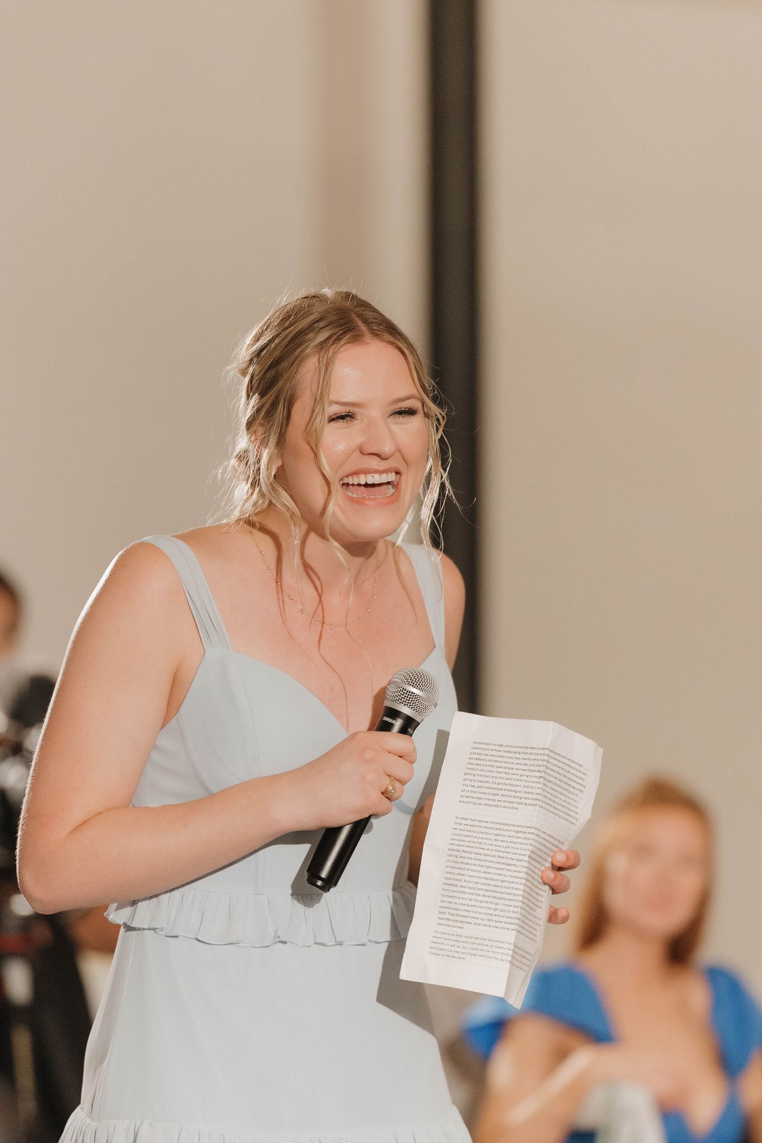 A person in a light blue dress holding papers delivers an emotional speech at a wedding reception.