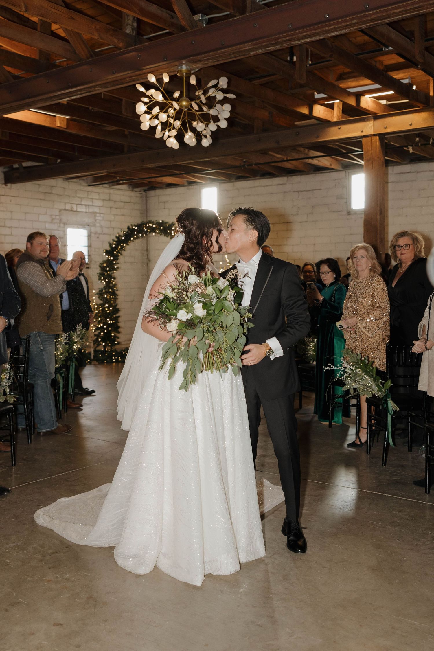 A couple celebrating their first dance at a rustic indoor wedding venue with exposed wooden beams and decorative lighting.