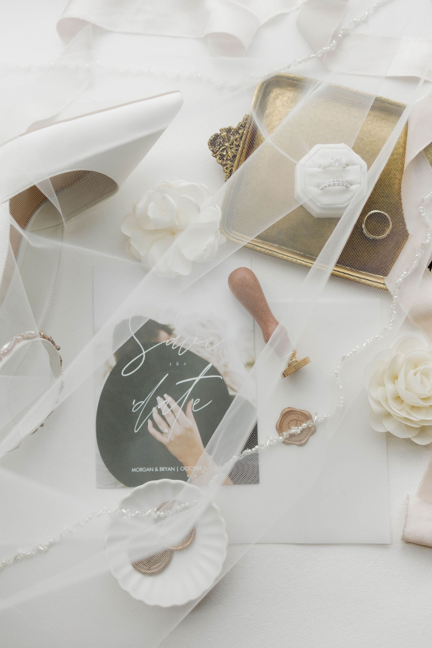 Wedding stationery and accessories arranged artistically on white background with flowing ribbons.